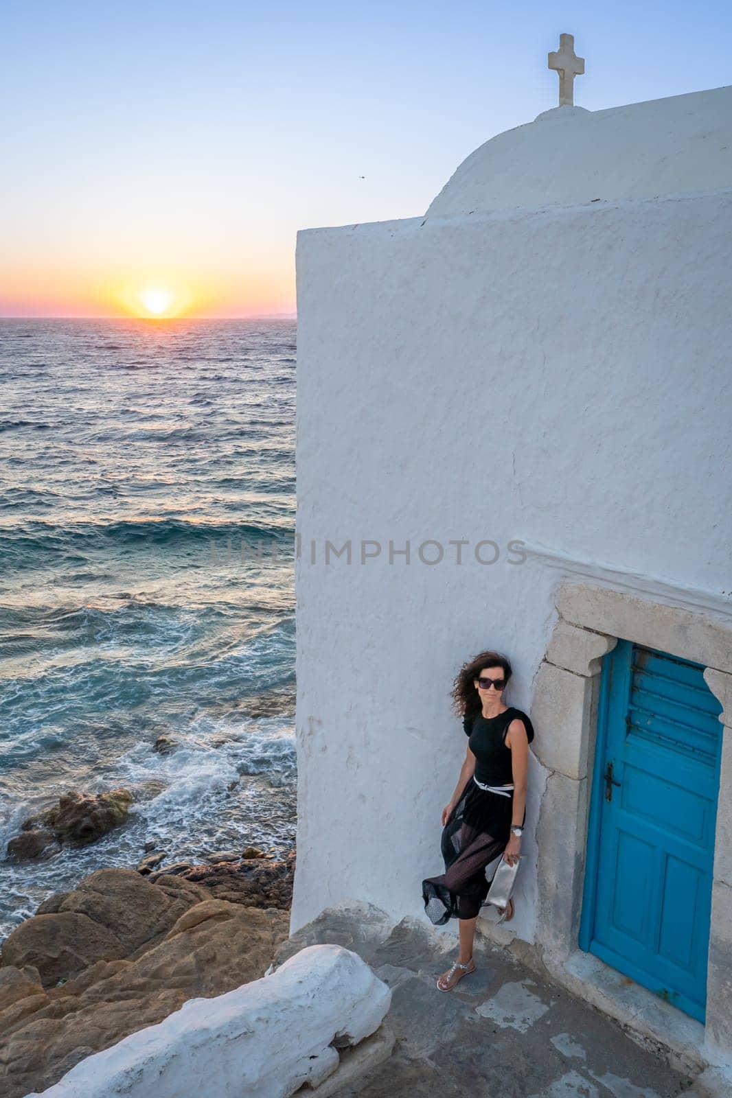 Young woman in black dress leaning on a wall at sunset in Mykonos