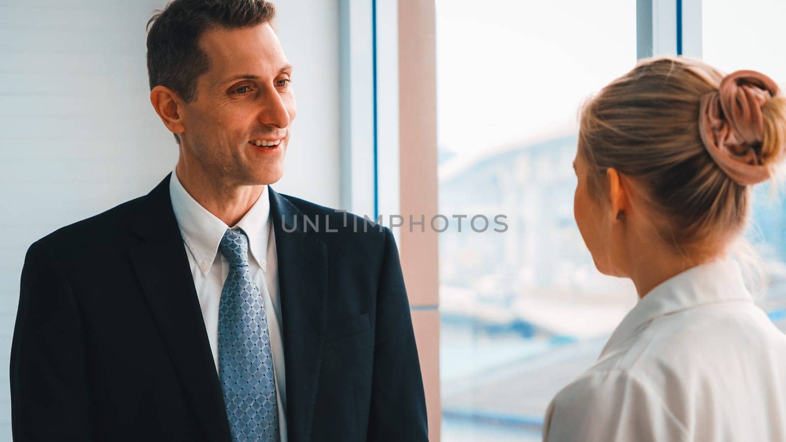 Two business people talk project strategy at office meeting room. Businessman discuss project planning with colleague at modern workplace while having conversation and advice on financial report. Jivy