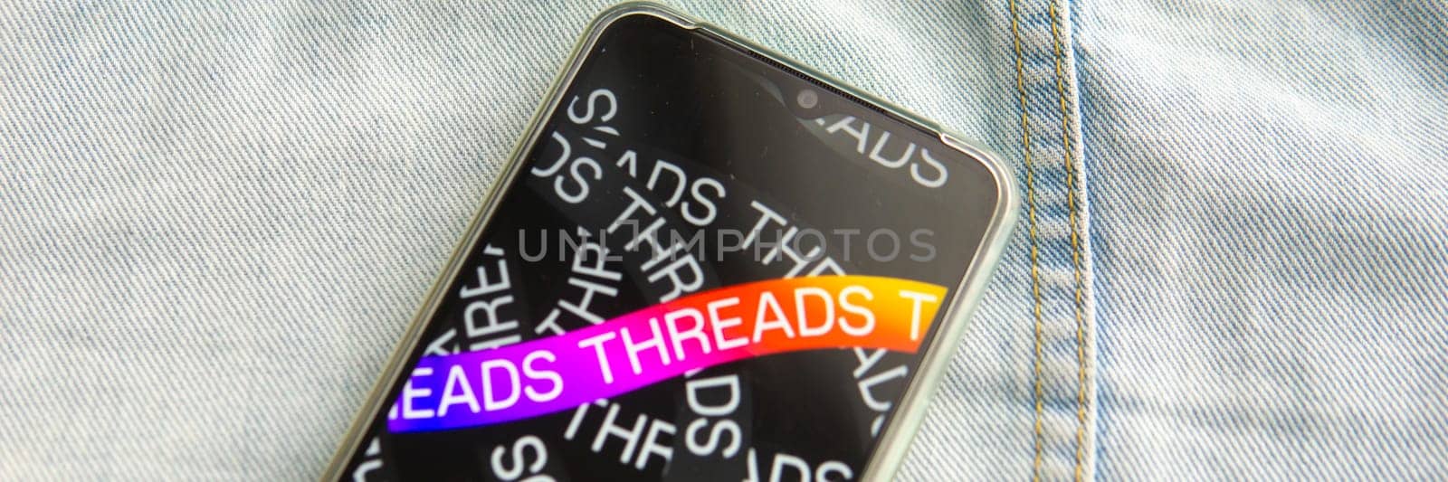 Tver, Russia - July 15, 2023, the threads logo on the smartphone screen lying on the jeans. The threads icon. The logo of the current application. Threads social network. by Annu1tochka