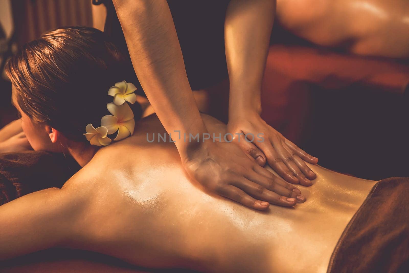Caucasian couple customer enjoying relaxing anti-stress spa massage and pampering with beauty skin recreation leisure in warm candle lighting ambient salon spa at luxury resort or hotel. Quiescent