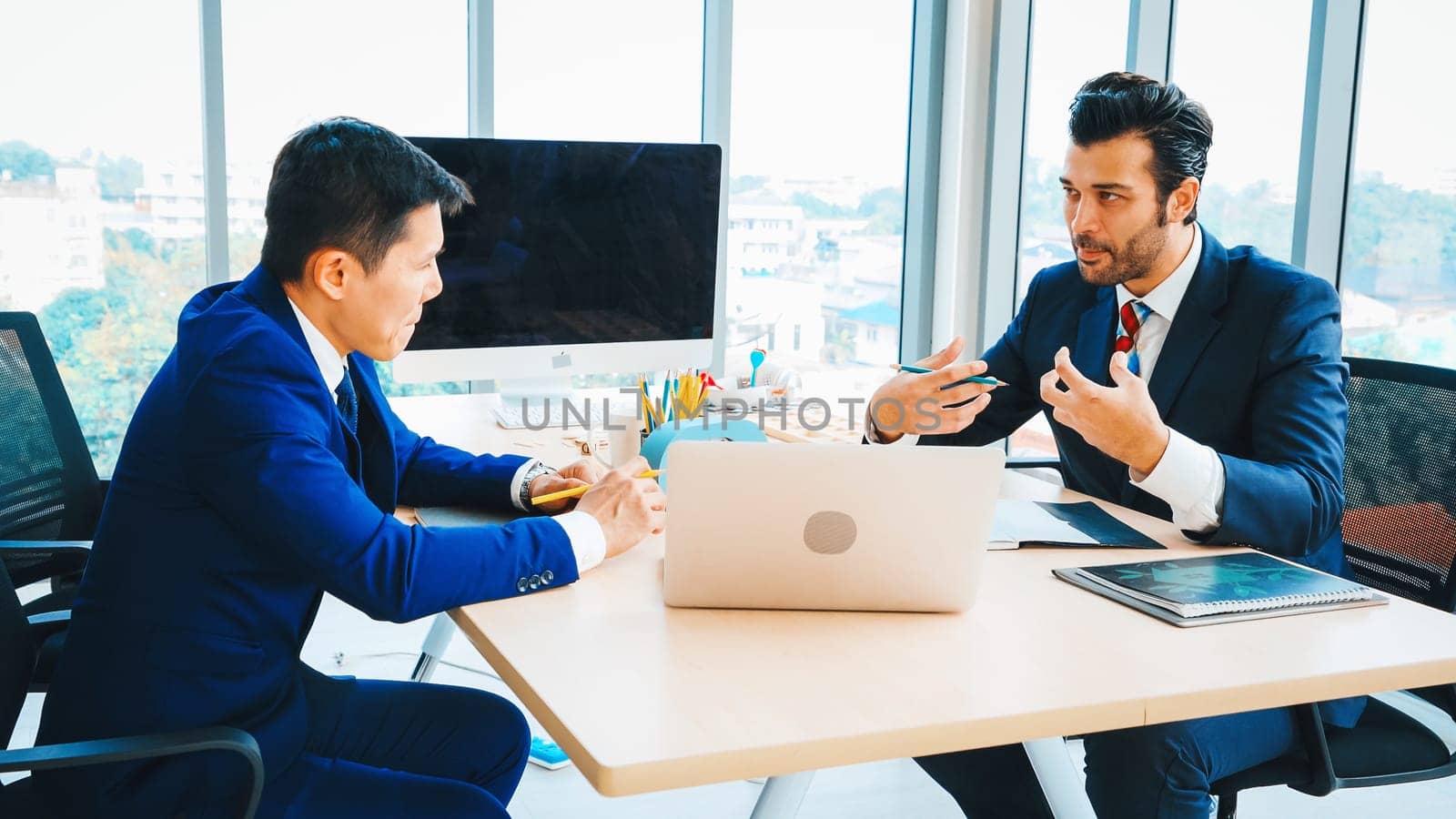 Two business people talk project strategy at office meeting room. Businessman discuss project planning with colleague at modern workplace while having conversation and advice on financial report. Jivy