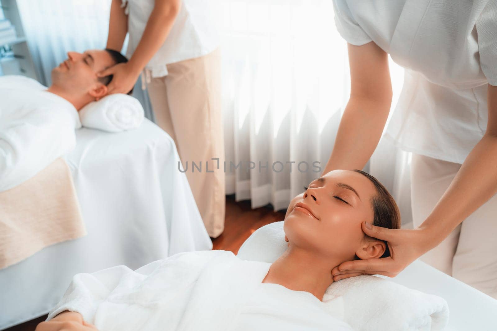 Caucasian couple enjoying relaxing anti-stress head massage and pampering facial beauty skin recreation leisure in dayspa modern light ambient at luxury resort or hotel spa salon. Quiescent