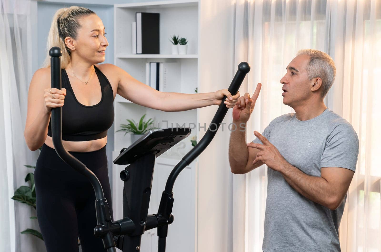 Active senior couple running on elliptical running machine at home together as fitness healthy lifestyle and body care after retirement for pensioner. Clout