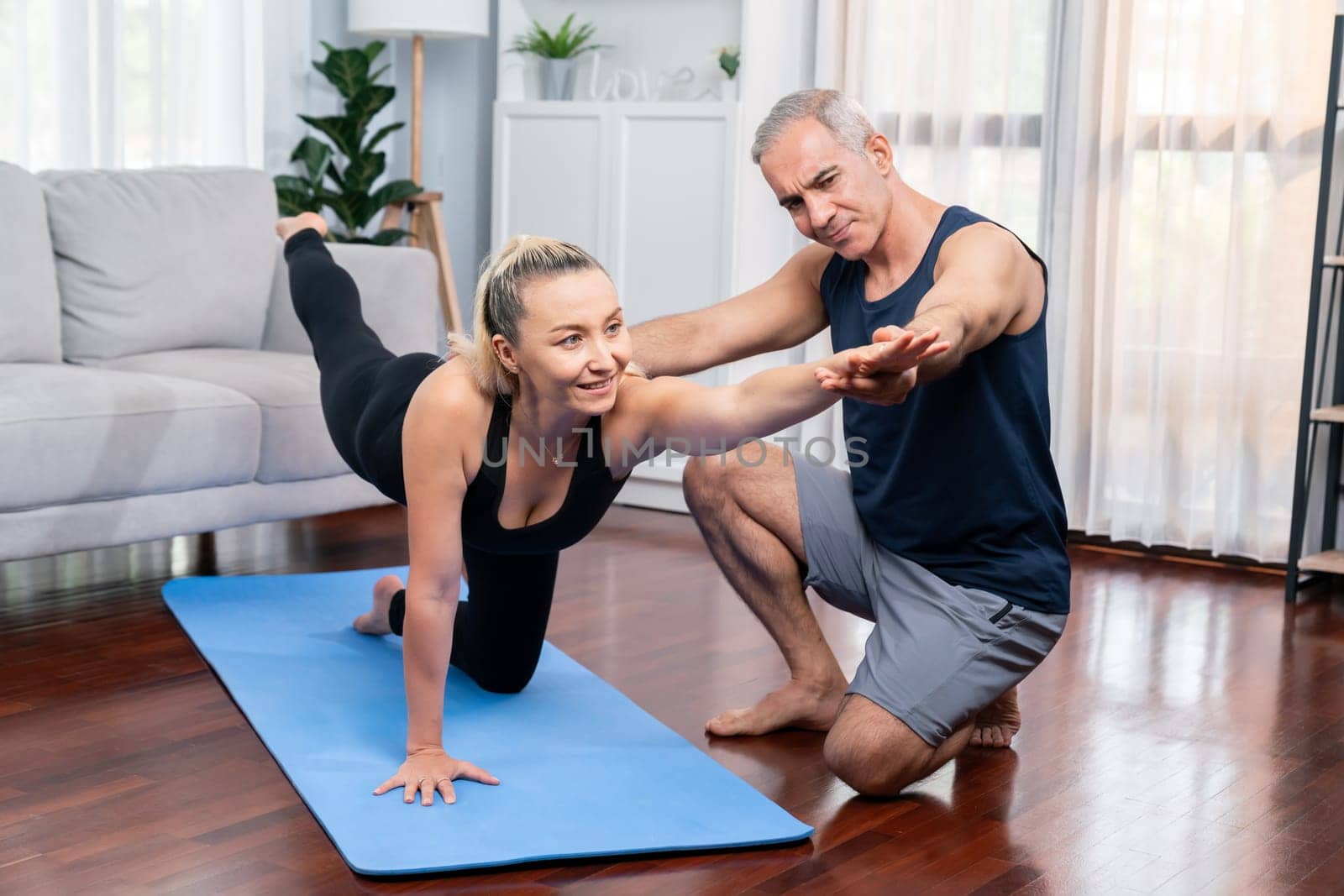 Happy active senior couple in sportswear being supportive and assist on yoga posture together at home. Healthy senior man and woman lifestyle with yoga exercise. Clout