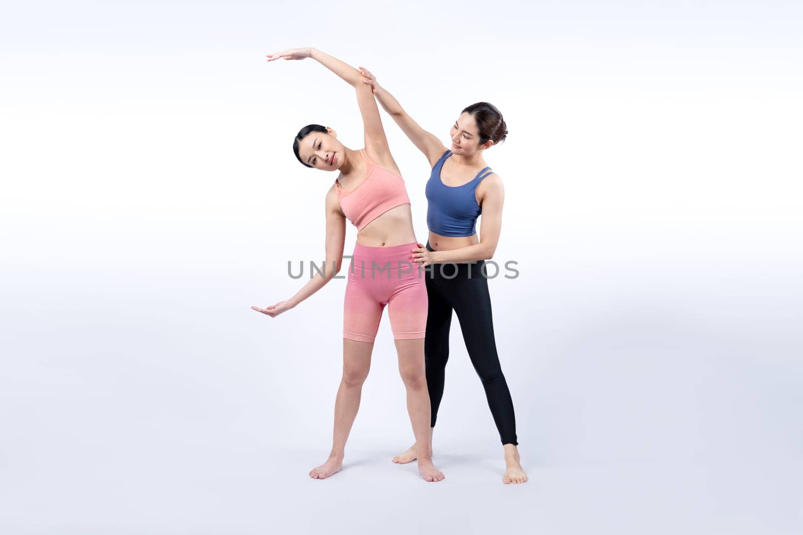 Asian woman in sportswear doing yoga exercise posing with trainer. Vigorous by biancoblue