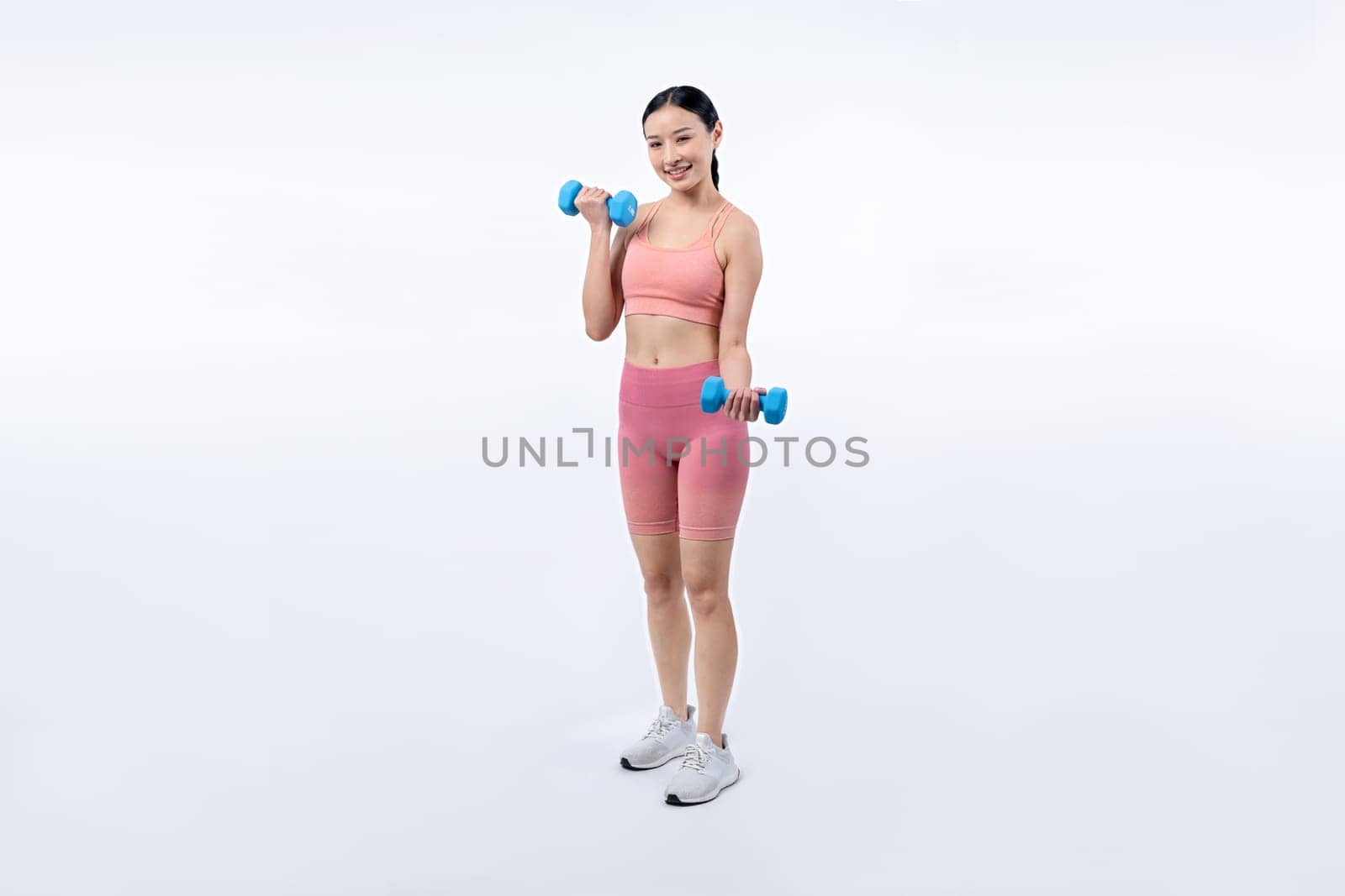 Vigorous energetic woman doing dumbbell weight lifting exercise on isolated background. Young athletic asian woman strength and endurance training session as body workout routine.