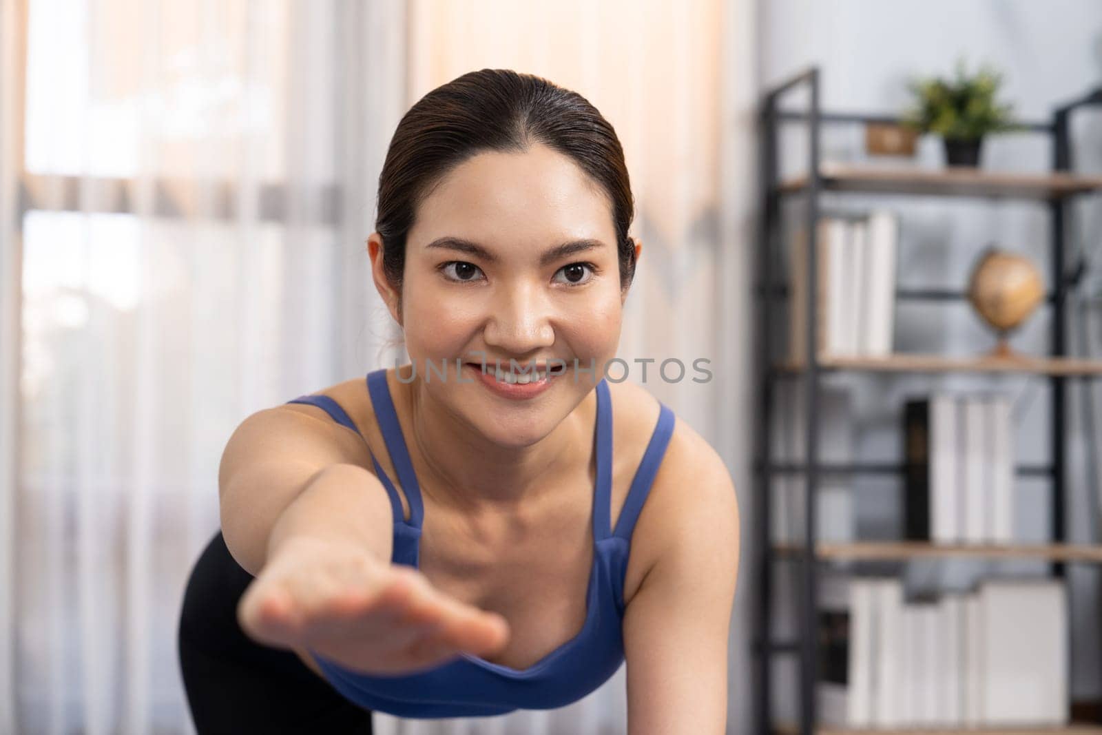 Asian woman in sportswear doing yoga exercise on fitness mat as her home workout training routine. Healthy body care and calm meditation in yoga lifestyle with comfortable and relaxation. Vigorous