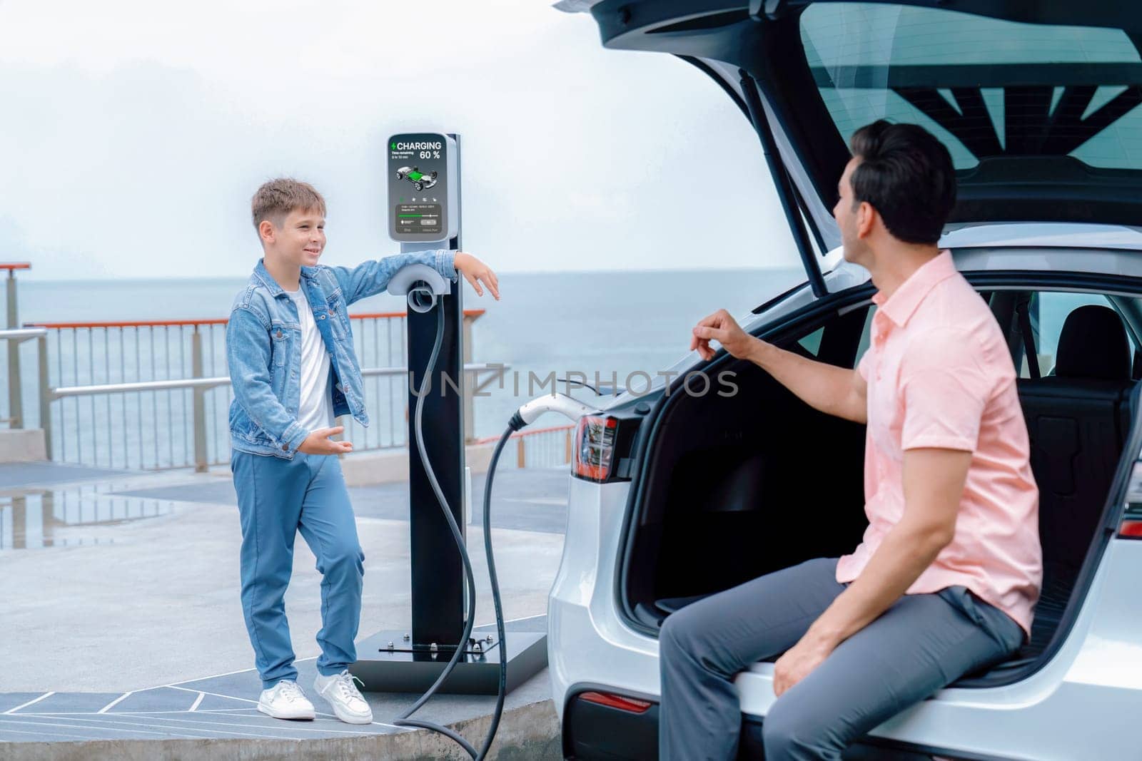 Family road trip vacation traveling by the sea with electric car, father and son recharge EV car with green and clean energy. Natural travel and eco-friendly car for sustainable environment. Perpetual