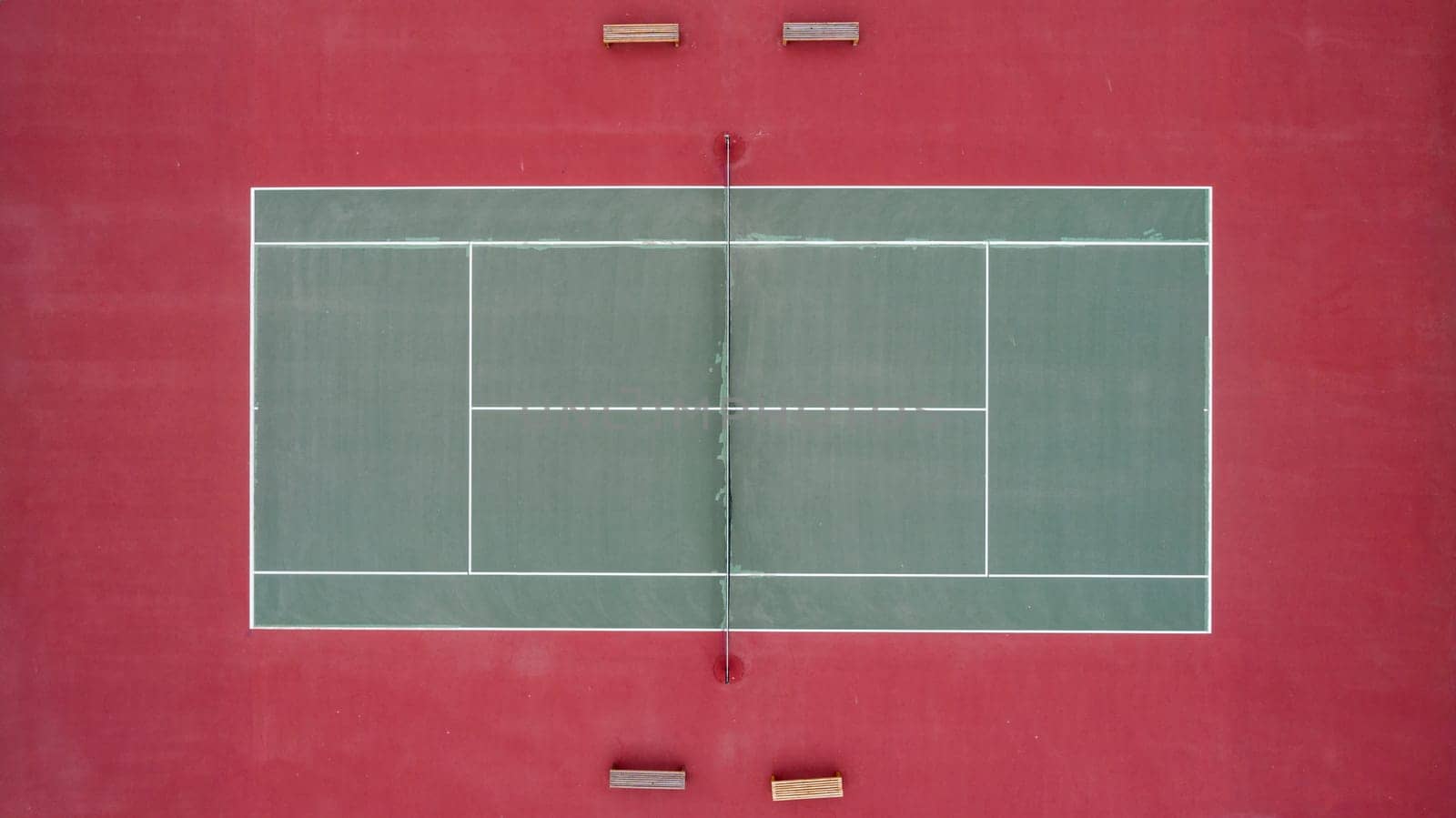 A tennis court with a net and two benches. The court is red and green