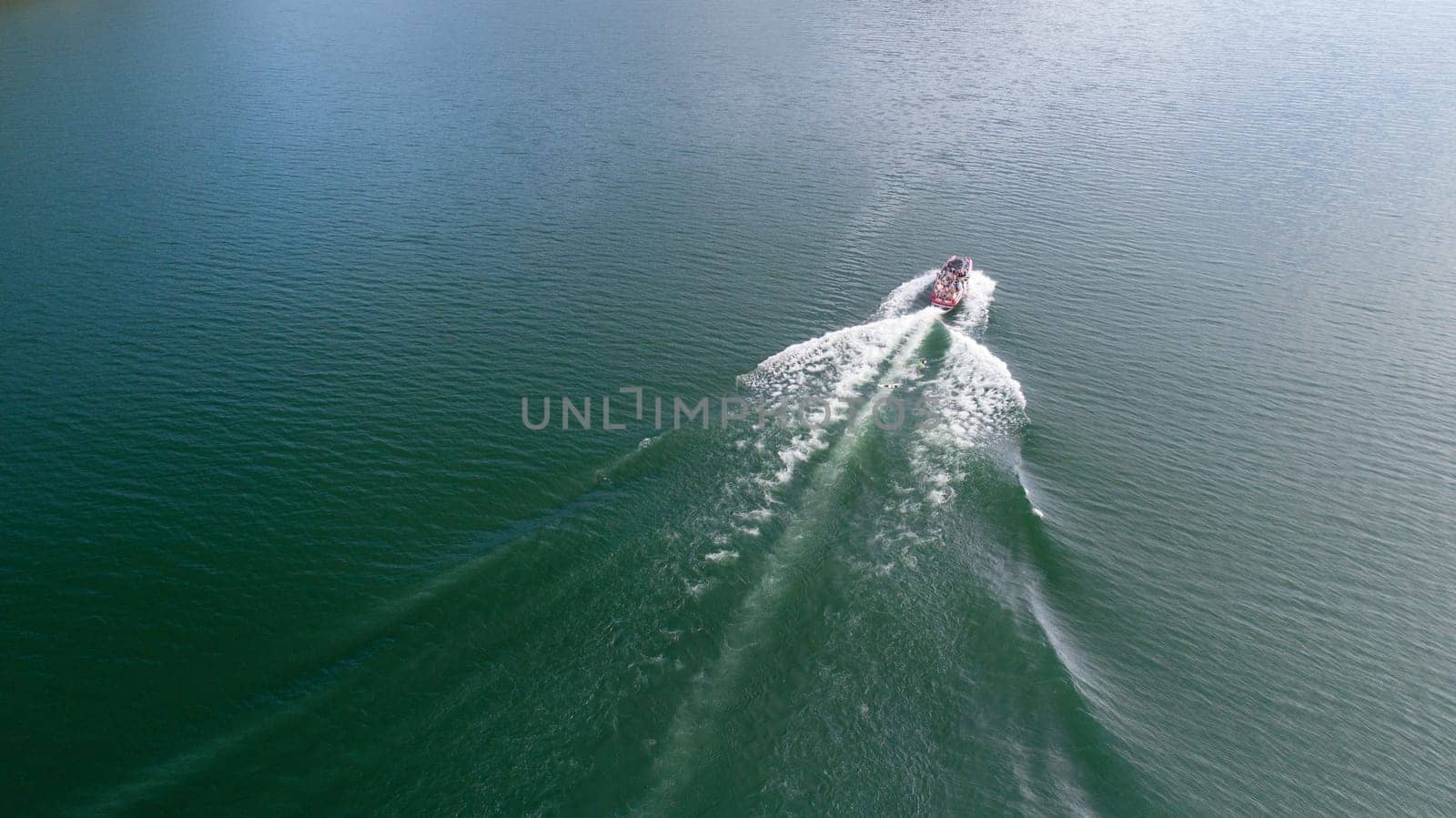 A boat is on the water with a wake behind it. The water is calm and the sky is clear