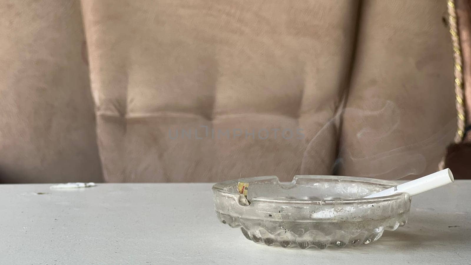 A cigarette rests in an ashtray, producing thin wisps of smoke, highlighting a cozy setting.