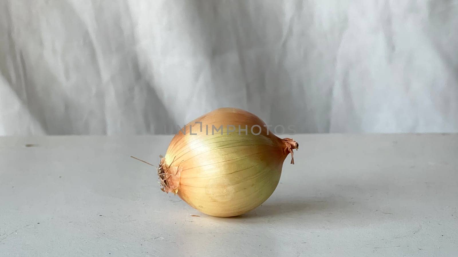 A single fresh onion sits on a smooth surface, ready for culinary use.
