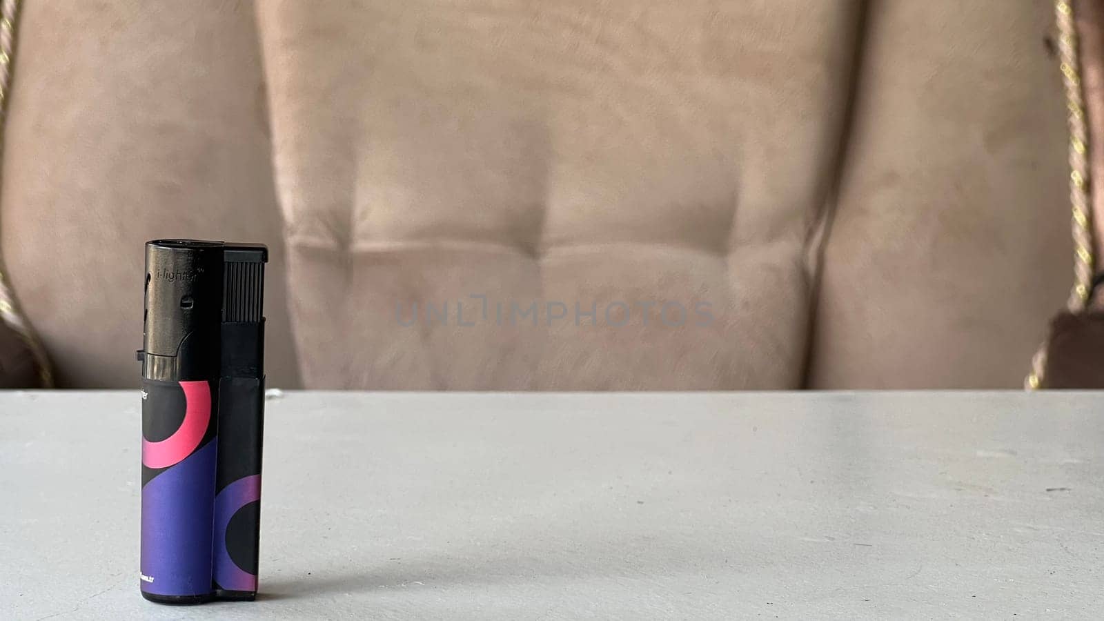 A colorful lighter stands on a table in front of a plush chair, suggesting indoor comfort.