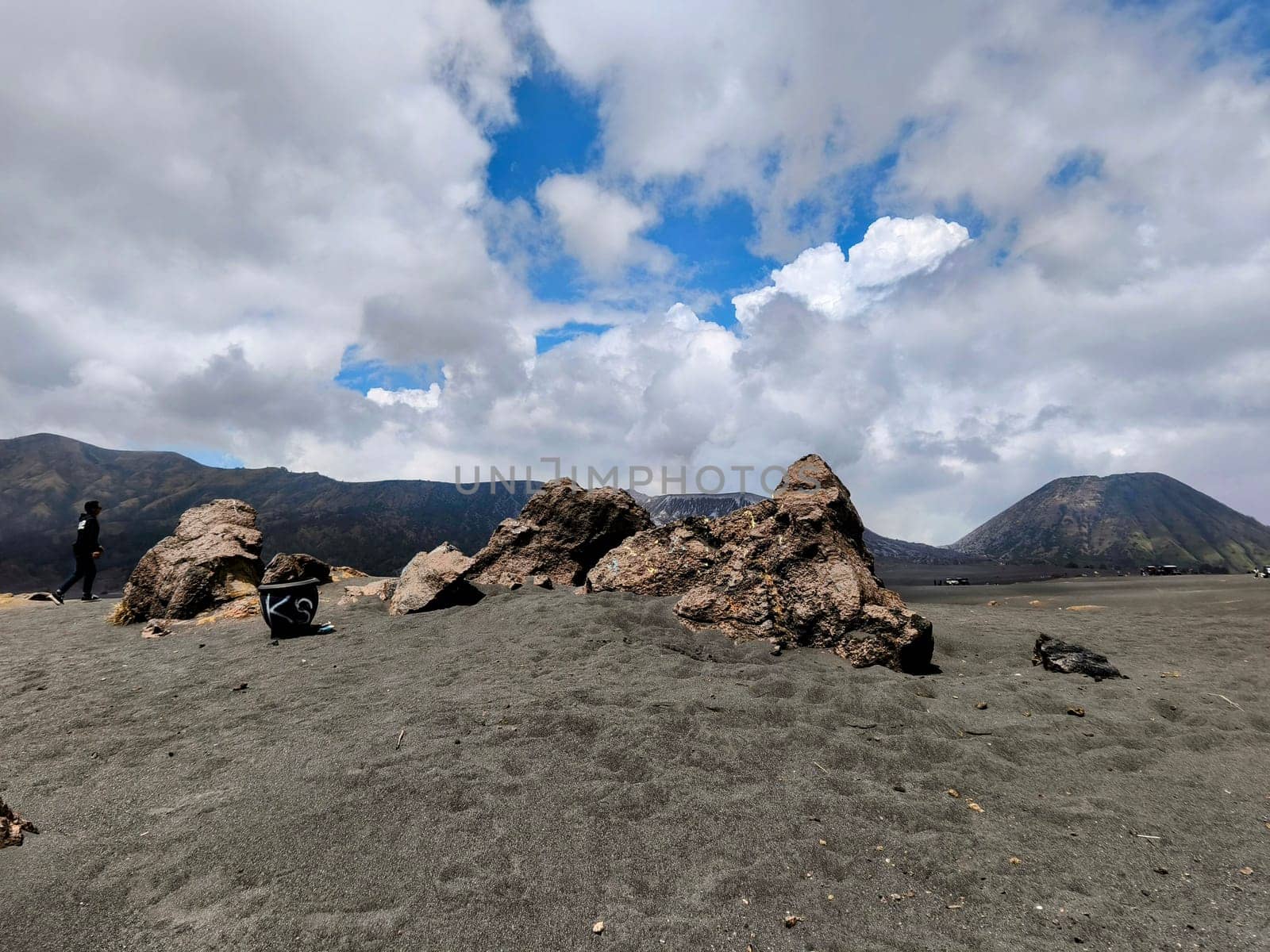 A breathtaking view of Mount Bromo, Indonesia. The volcano's peak is shrouded in dramatic clouds, creating a sense of awe and mystery. The foreground features a rocky landscape