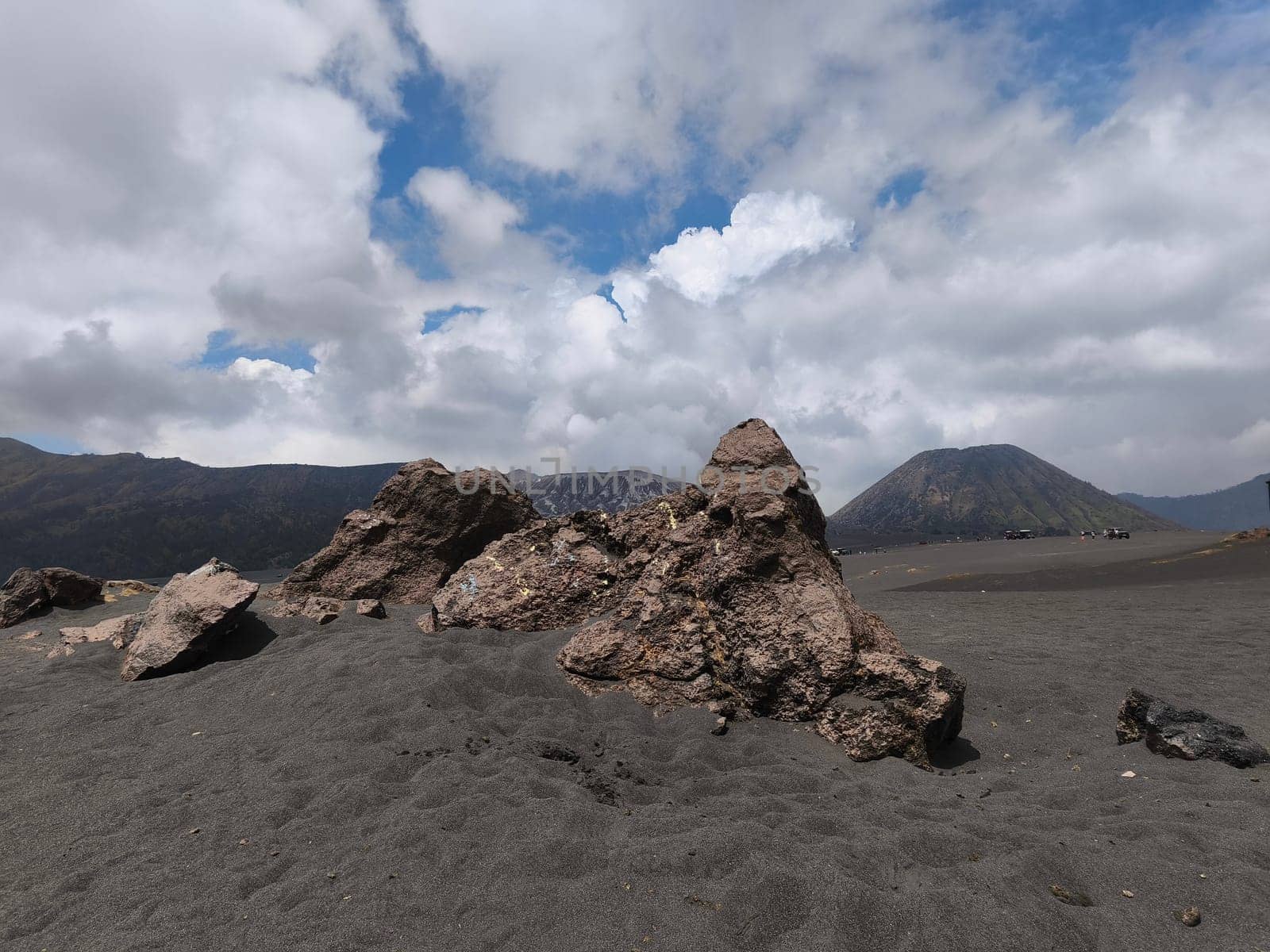 A breathtaking view of Mount Bromo, Indonesia. The volcano's peak is shrouded in dramatic clouds, creating a sense of awe and mystery. The foreground features a rocky landscape