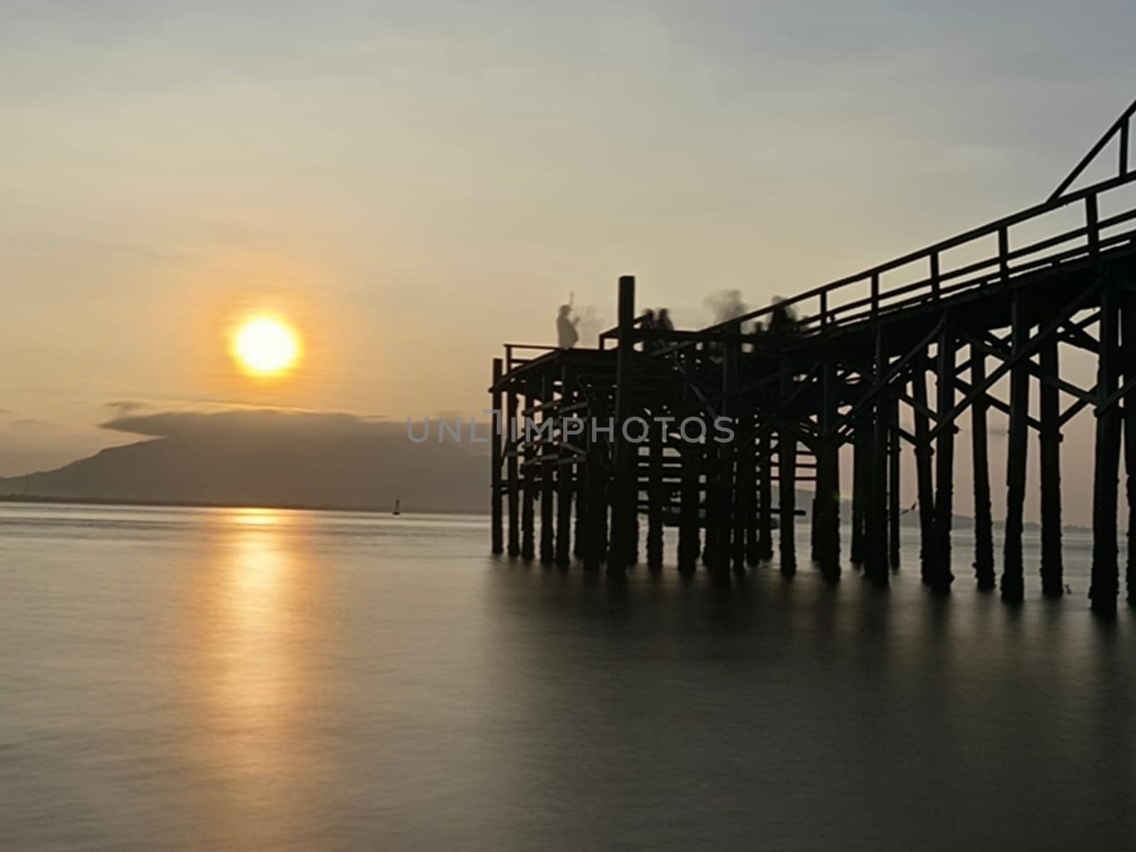 A weathered wooden pier extends into the water at sunrise, with barnacles clinging to the support posts near Banyuwangi, Indonesia