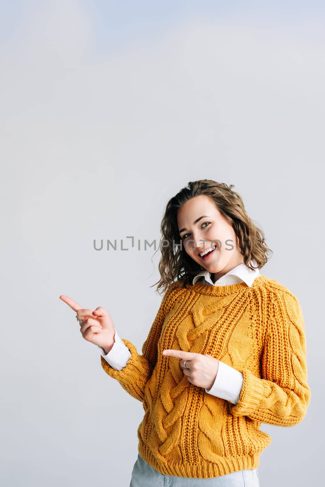 Young woman with curly hair, smiling and pointing excitedly to the side. Perfect for showcasing promotions, sales, or special offers. on a white background, ideal for marketing and advertising themes.