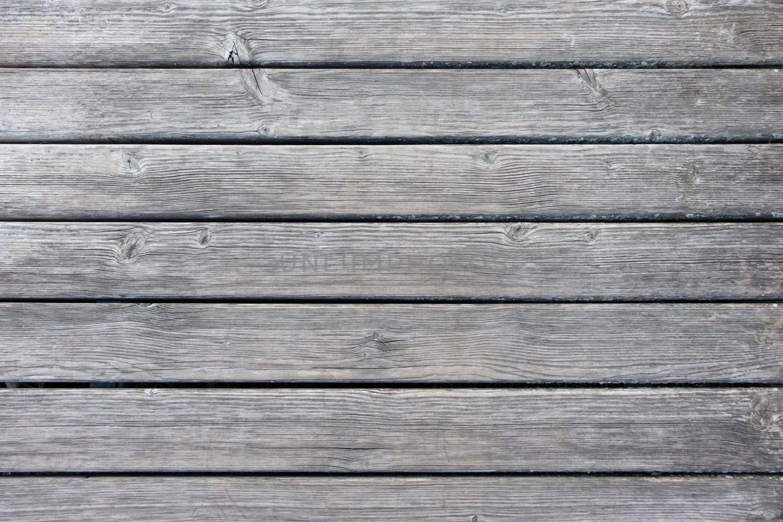 A high-resolution view of wooden plank flooring showing natural grain patterns, subtle color variations, and weathered details. The horizontal arrangement of planks offers a rustic, natural aesthetic ideal for backgrounds or interior design themes.