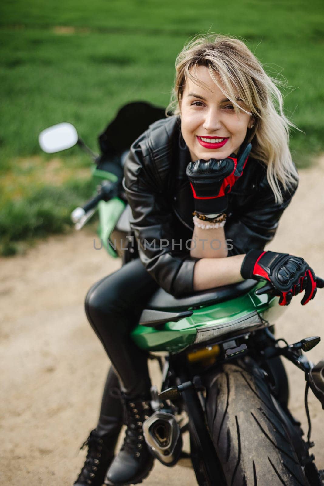 A woman in a black leather jacket and pants sits on a green motorcycle. She wears a red glove on her left hand, capturing a bold and adventurous style. Ideal for themes of motorcycling and freedom.