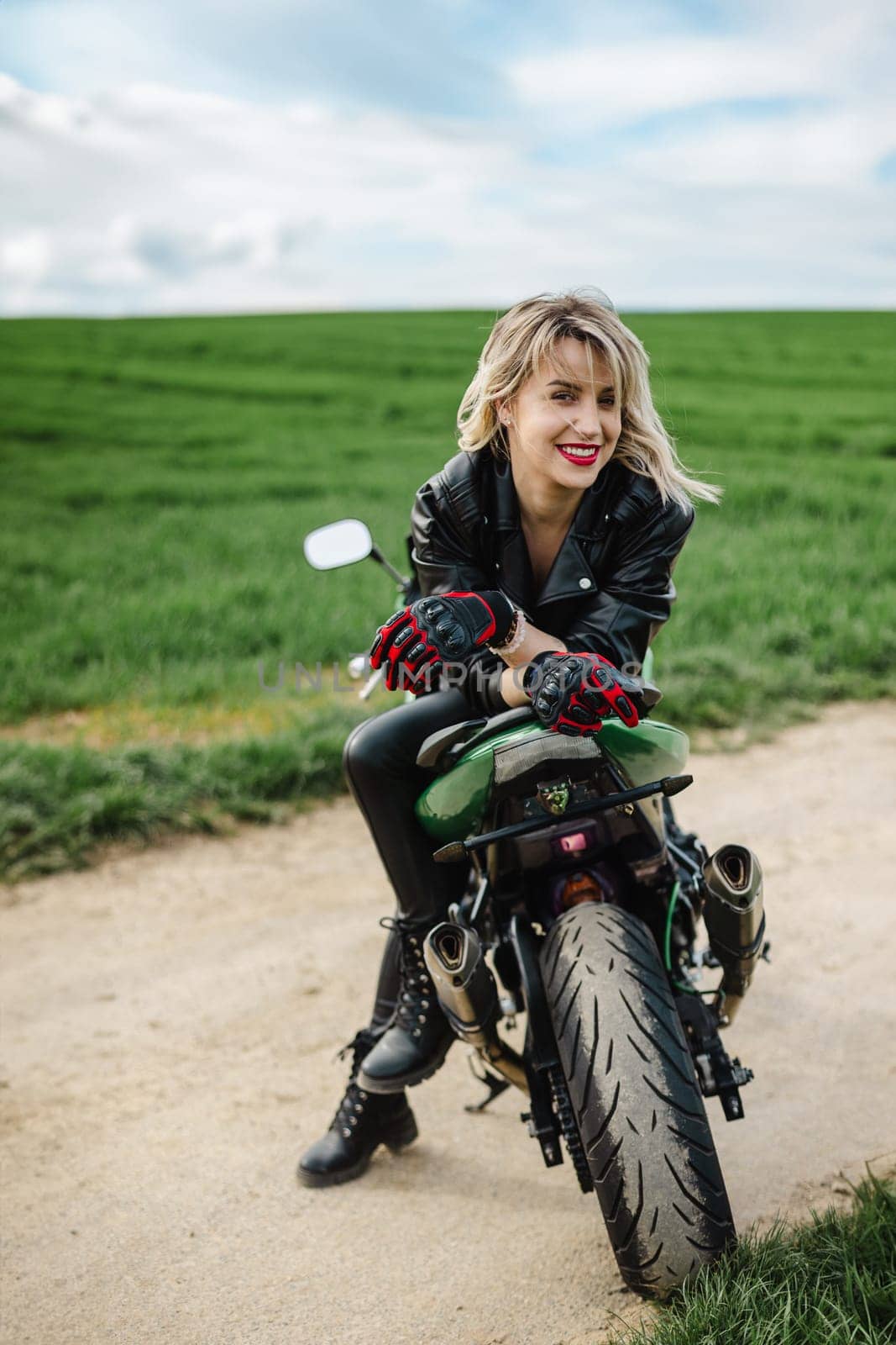 Woman in Leather Jacket Sitting on Motorcycle. Confident woman seated on motorcycle, wearing black leather jacket and gloves, with a focused look. Scene captures a sense of adventure