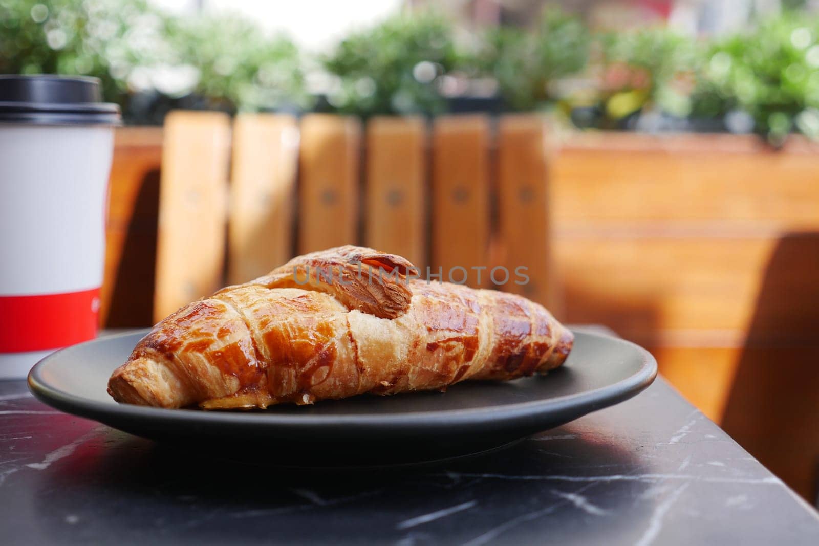 A delightful flaky croissant beautifully served on a plate alongside a warm coffee cup