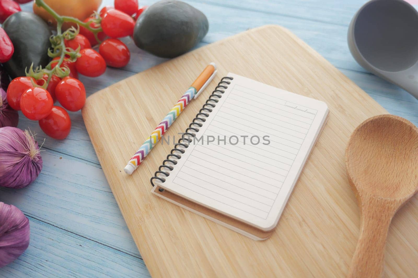 A notebook and colorful pen next to fresh vegetables on a wooden cutting board, ready for cooking