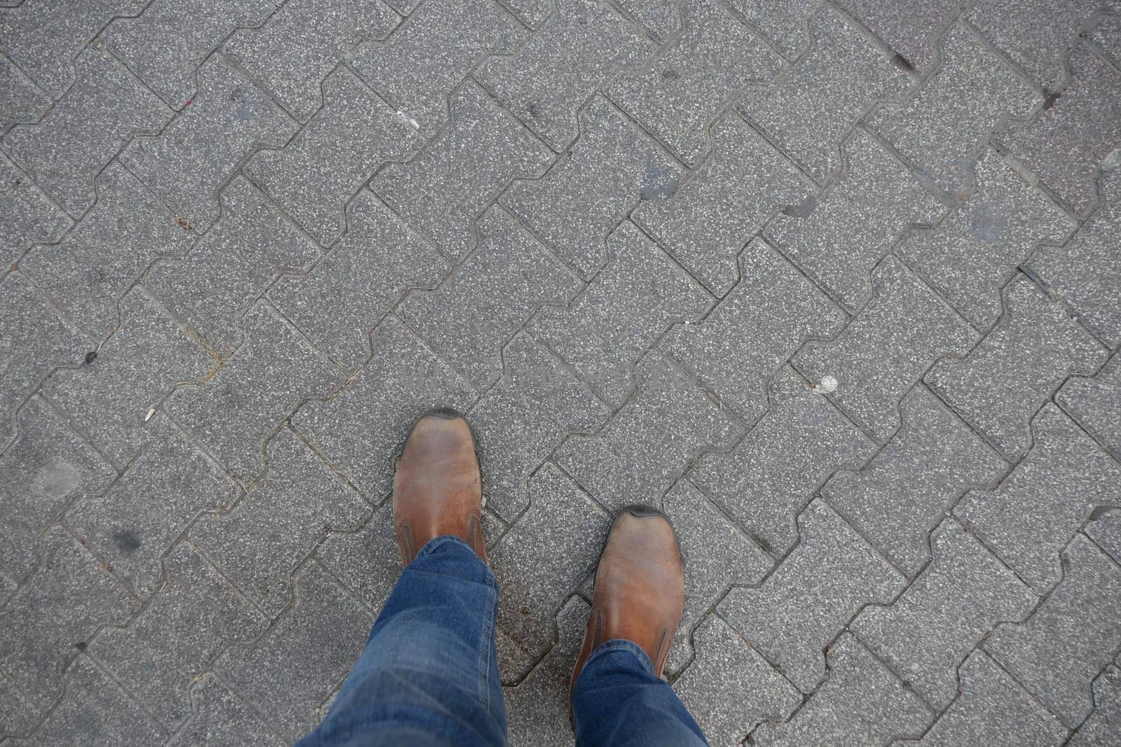 A stylish pair of brown shoes on patterned stone pavement, paired with denim jeans