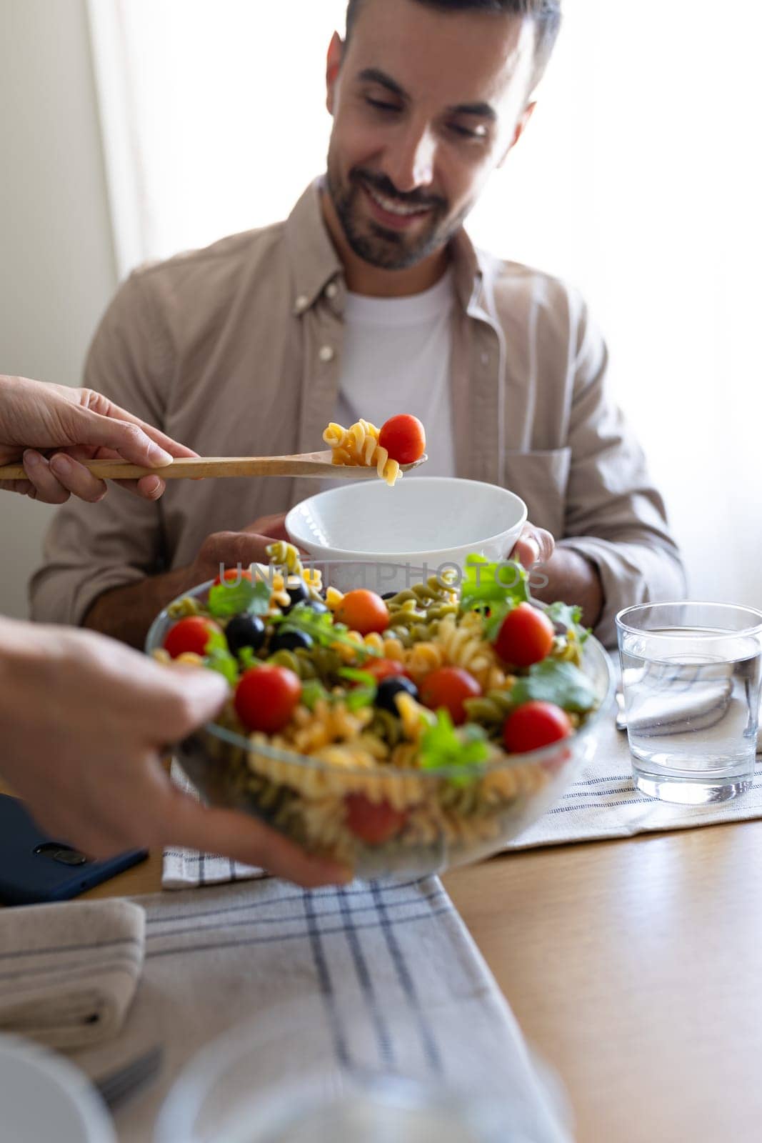 Close up of woman serving pasta salad to husband. Married couple having meal together at home dining table. Vertical. Lifestyle concept.