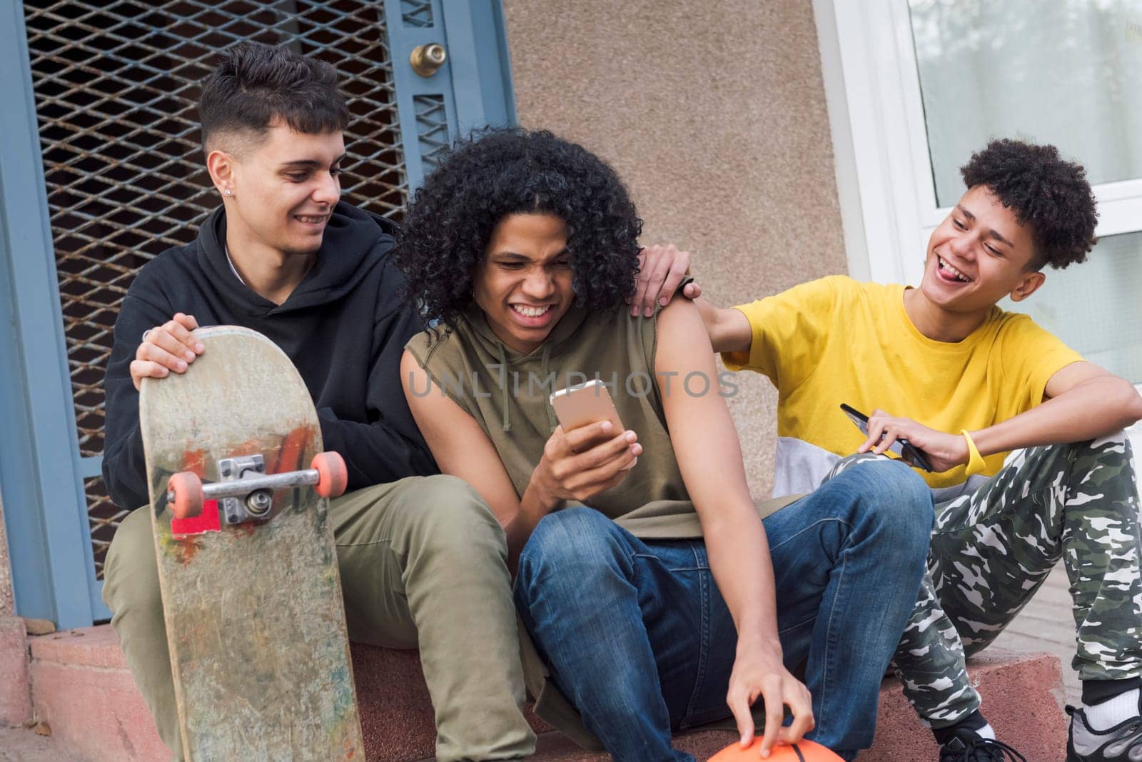 three happy multiethnic teen friends having fun sharing mobile phone sitting together with on street, concept of youth and technology of communication