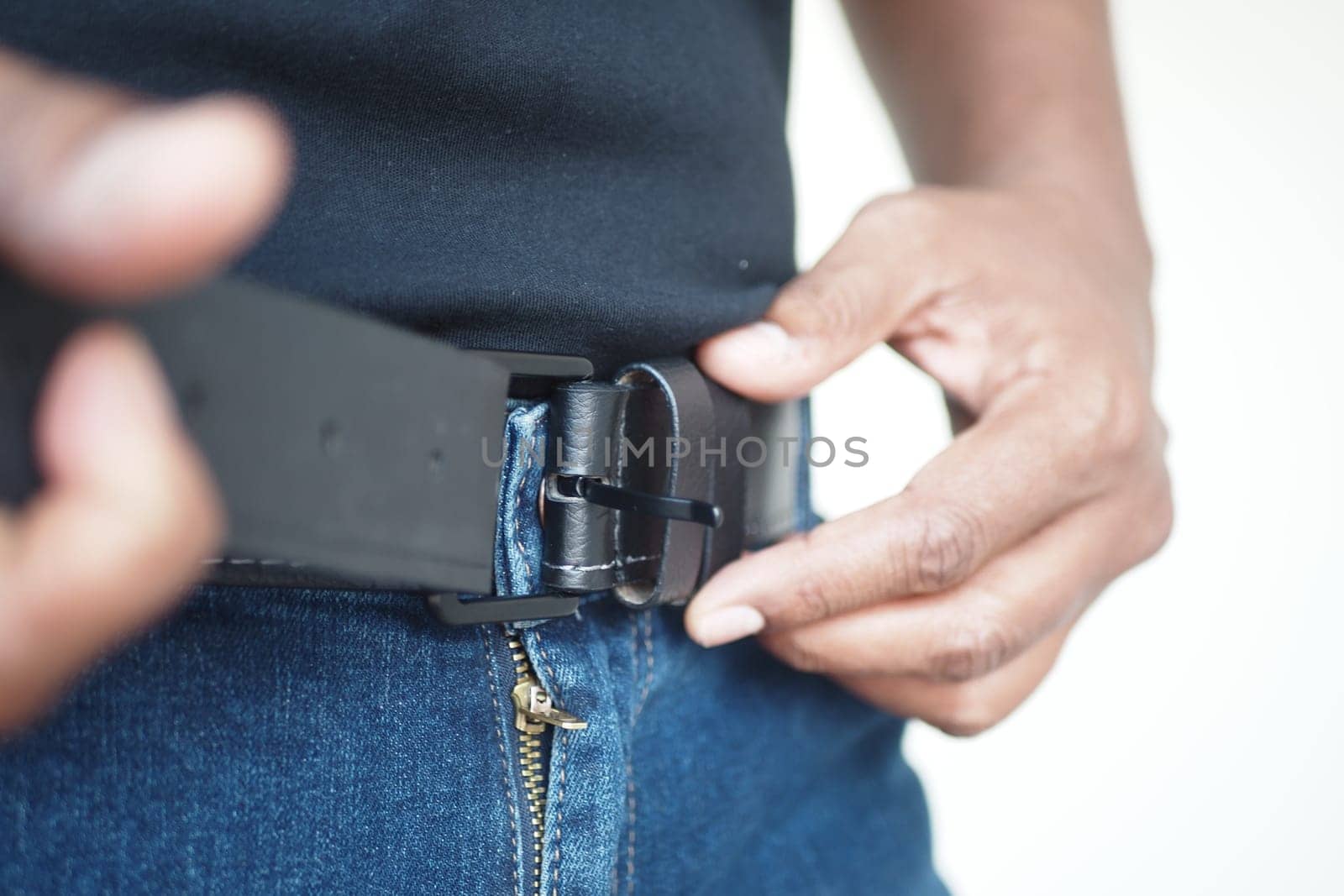 A person is fastening a black belt around their waist while wearing stylish jeans
