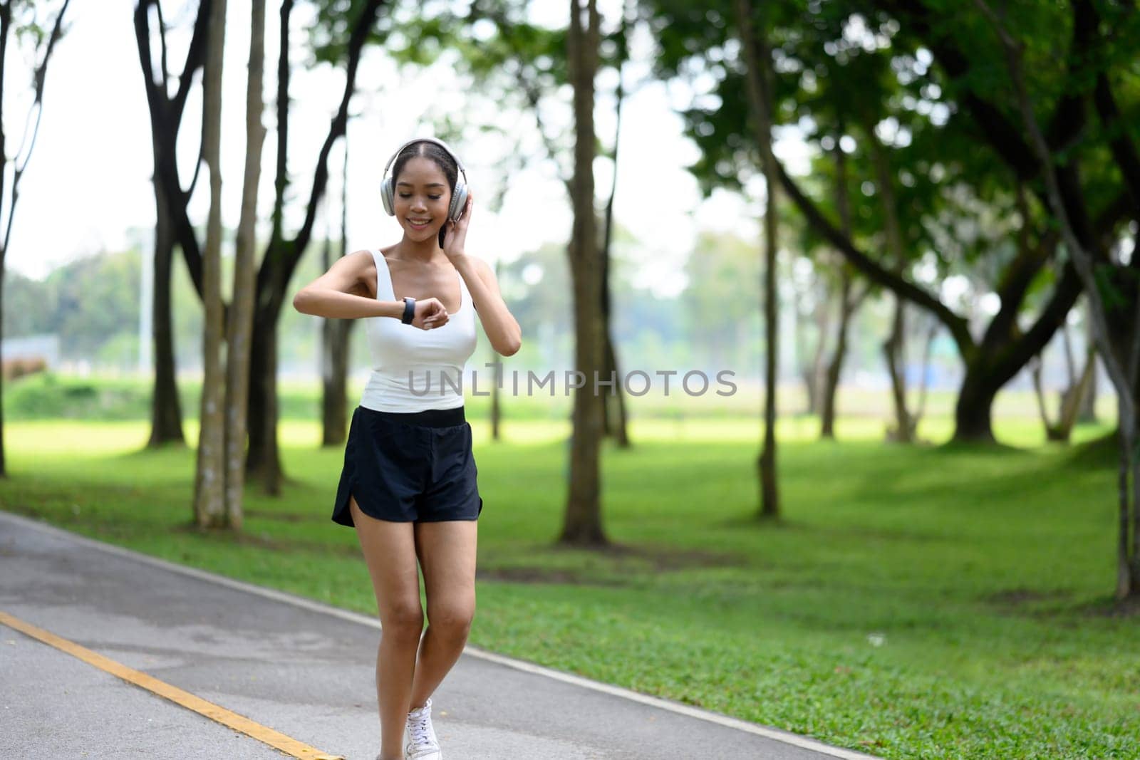 Smiling young woman checking her fitness data on smartwatch while jogging in a park.