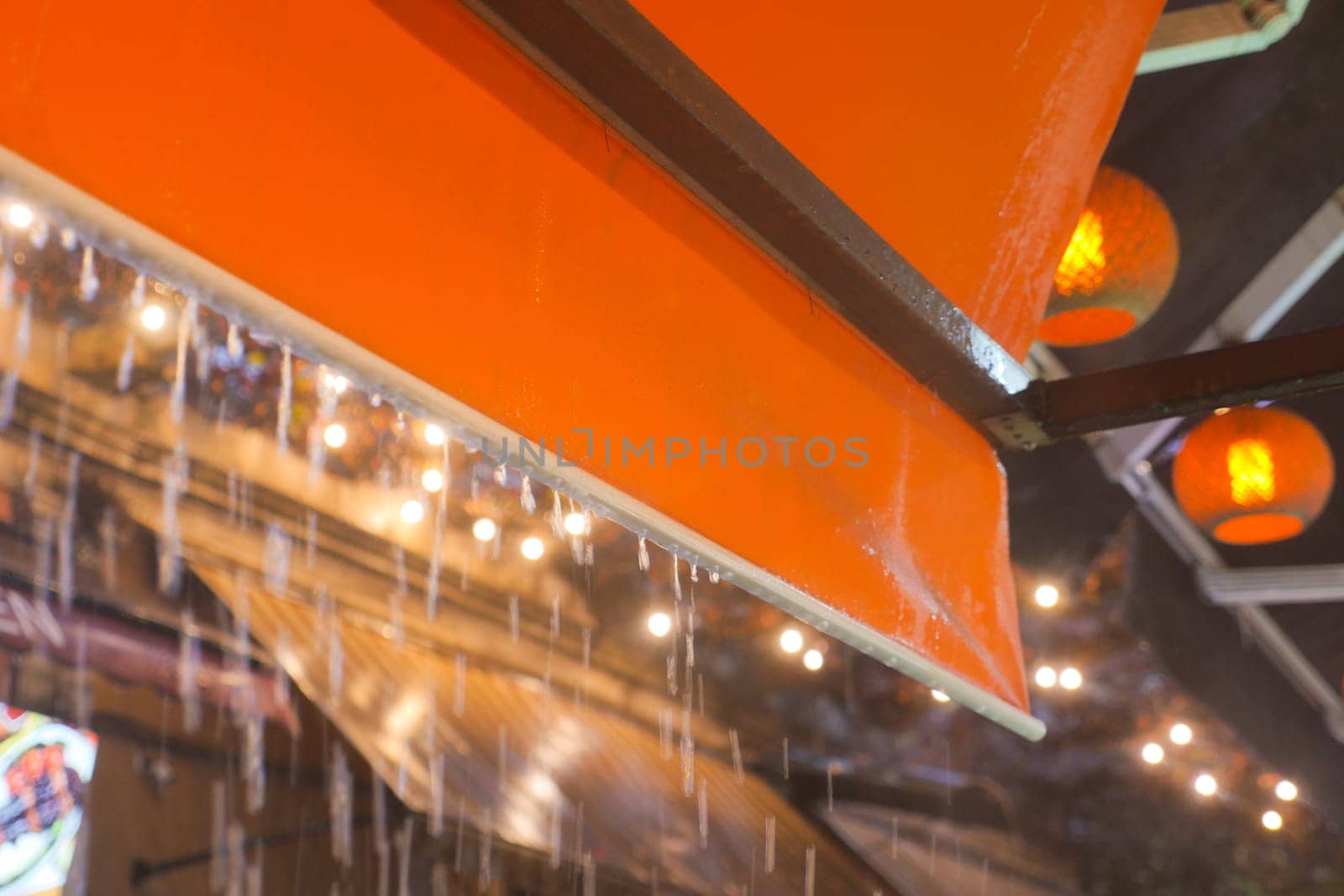 An orange canopy overhead draped in gentle rain, with lanterns and soft lights creating warmth