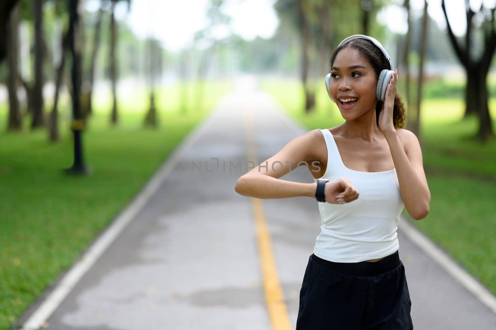Cheerful young sportswoman monitoring her progress on a smartwatch while jogging through a peaceful park.
