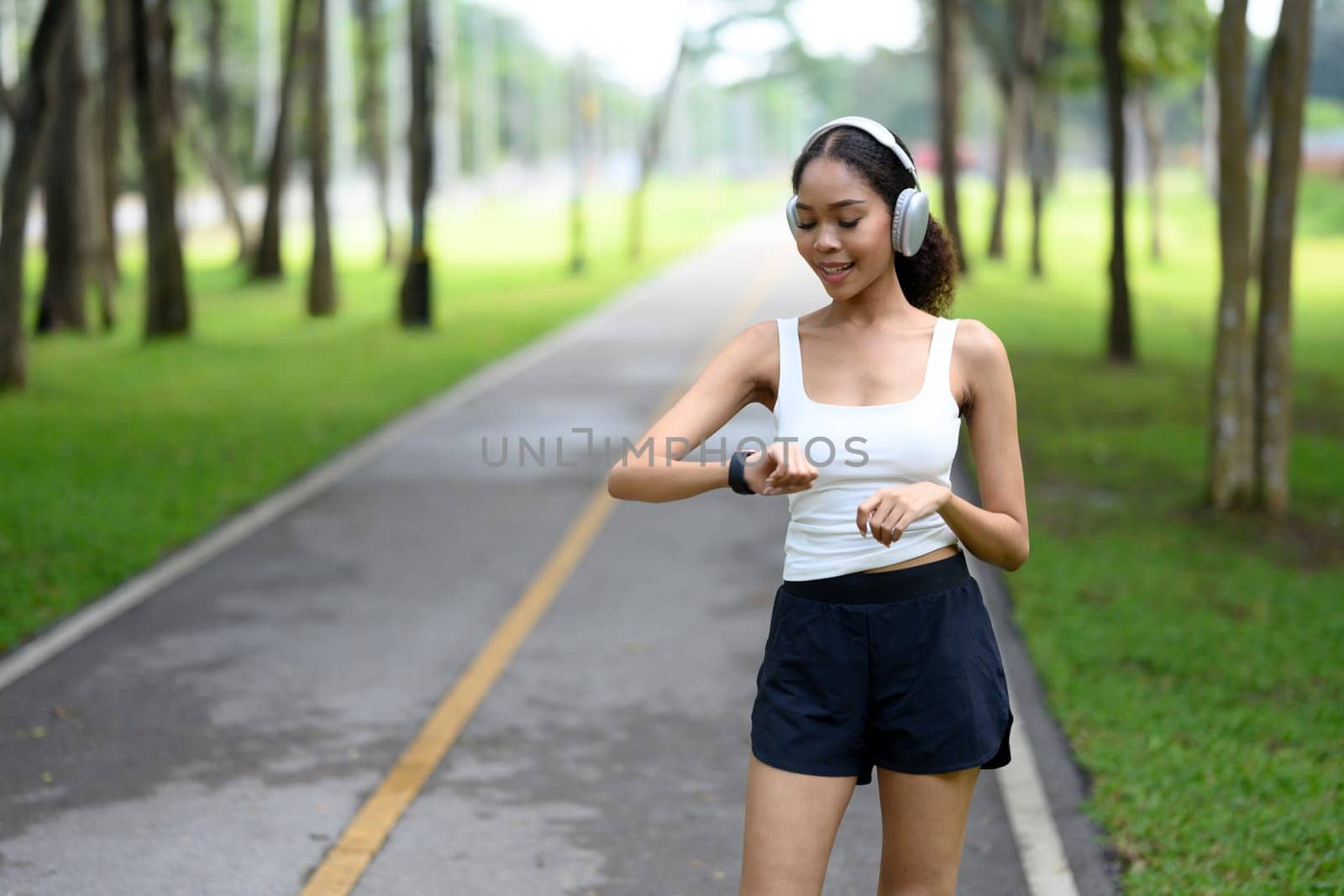 Happy African American woman checking her fitness tracker during a jog in the park,.