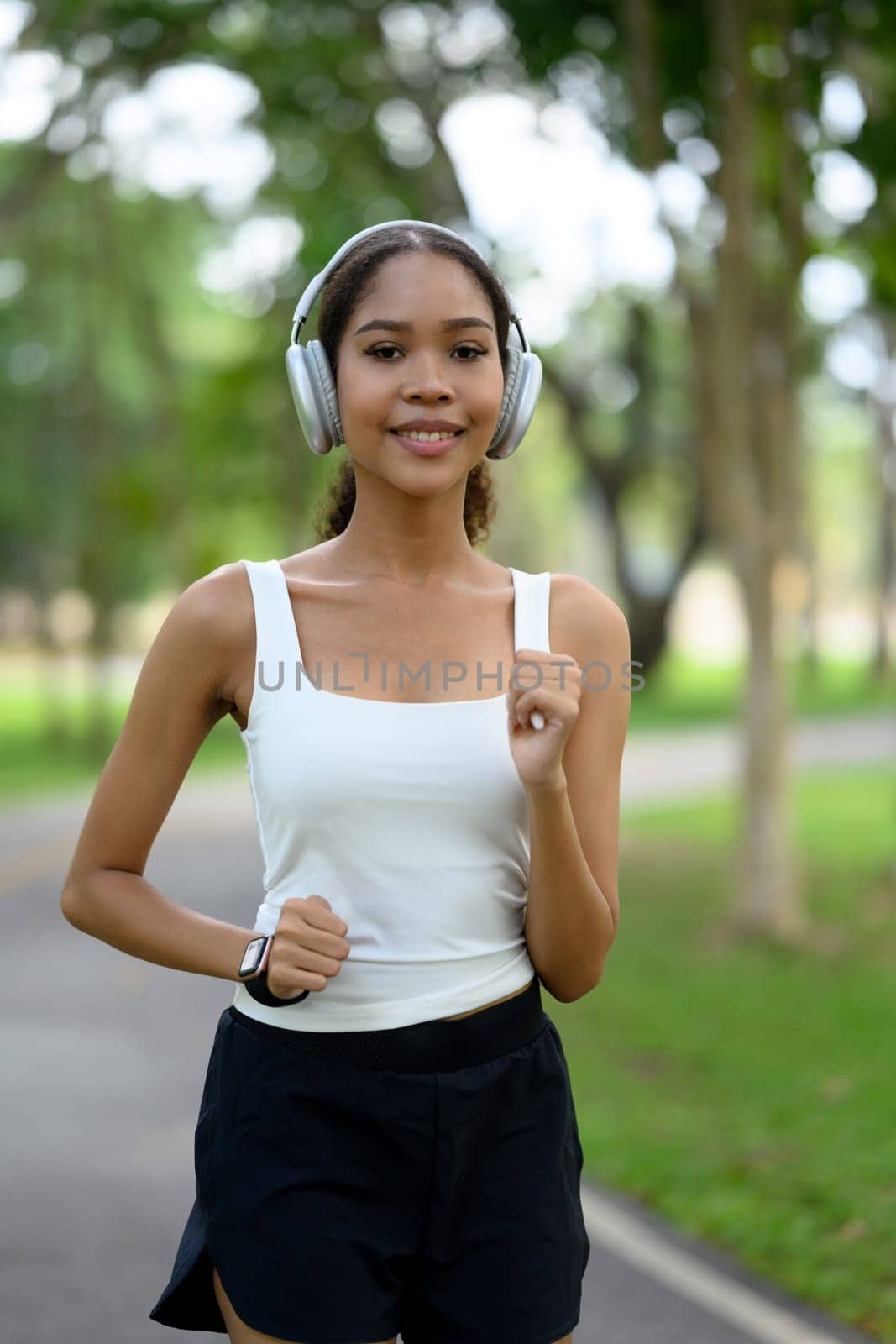 Young African American woman with headphones jogging through a green park.