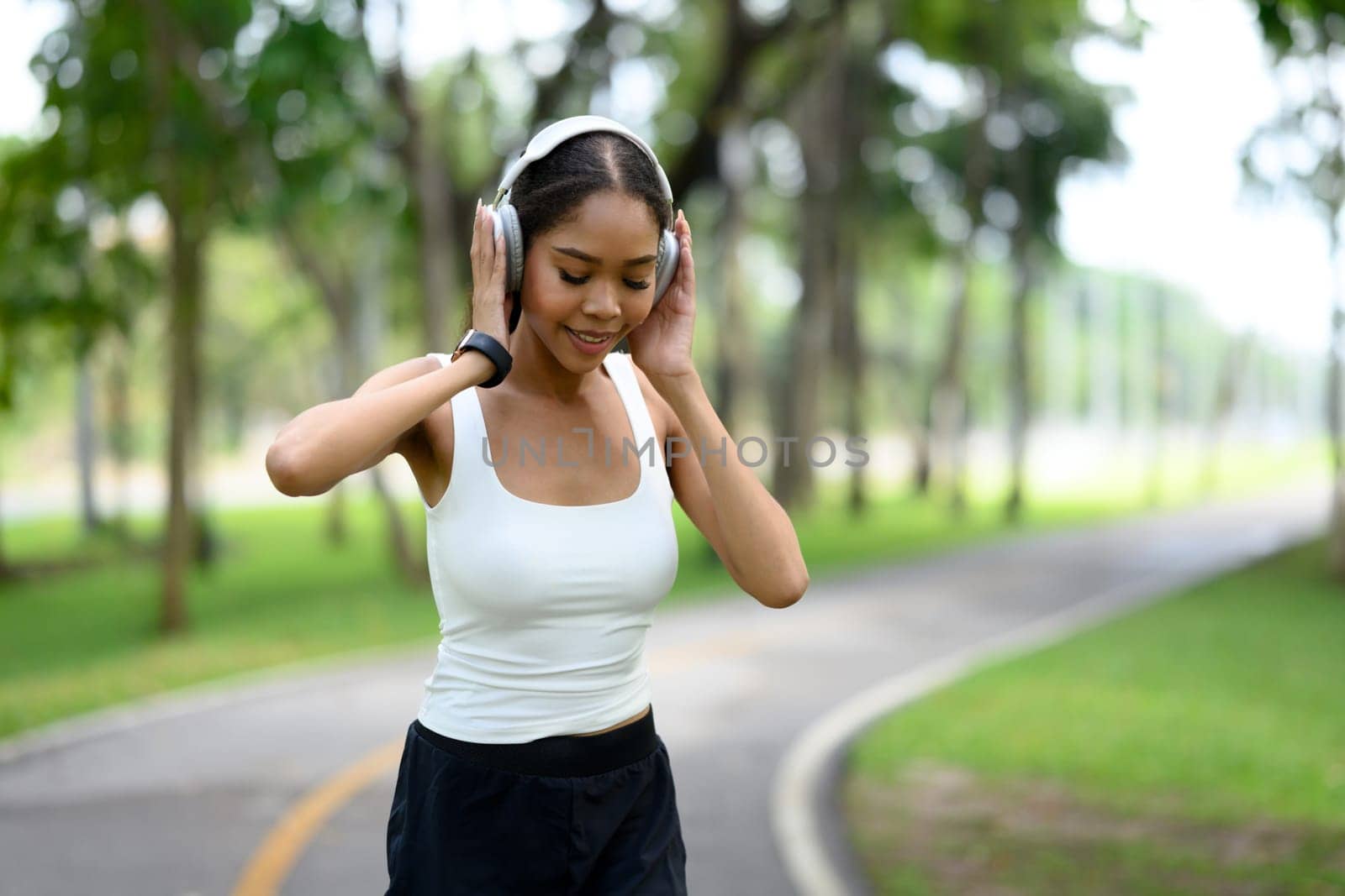 Happy athletic female jogging in the park while listening to music through headphones.