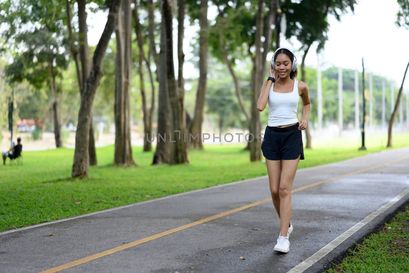 Sporty young woman with headphones jogging along a park path.