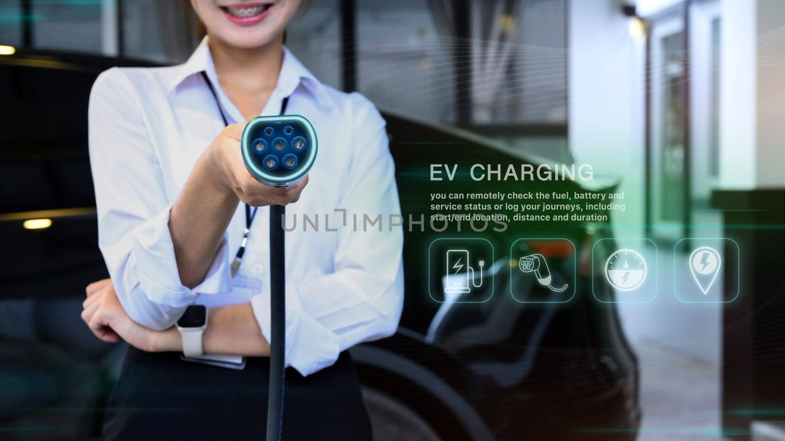 Smiling woman holding an EV charger with digital interface display to check real time data on the vehicle battery.
