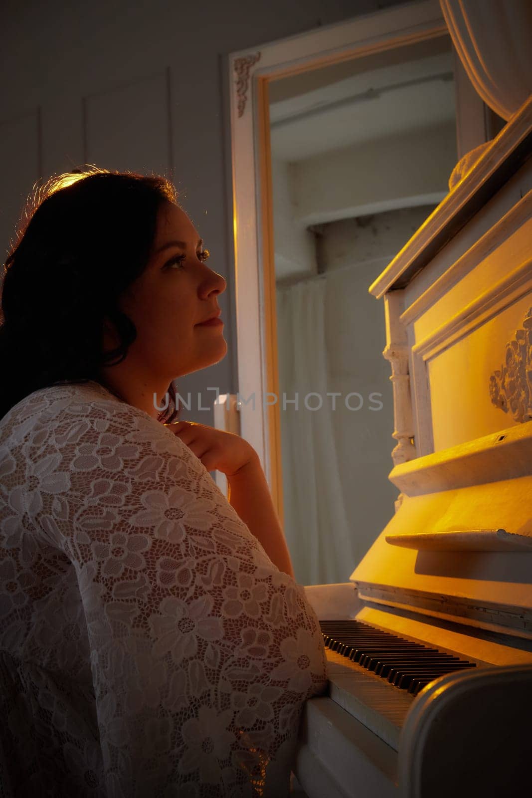 A woman in a delicate dress sits beside a piano, lost in thought as warm light enhances the romantic atmosphere of the setting.