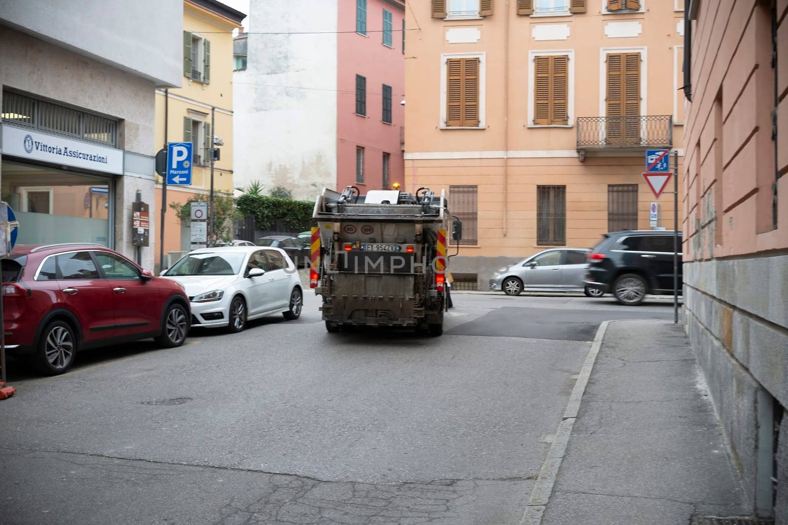 Cremona, Lombardy, Italy - October 27th 2024 Garbage truck maneuvering on a narrow street, passing parked cars, during garbage collection in an urban area