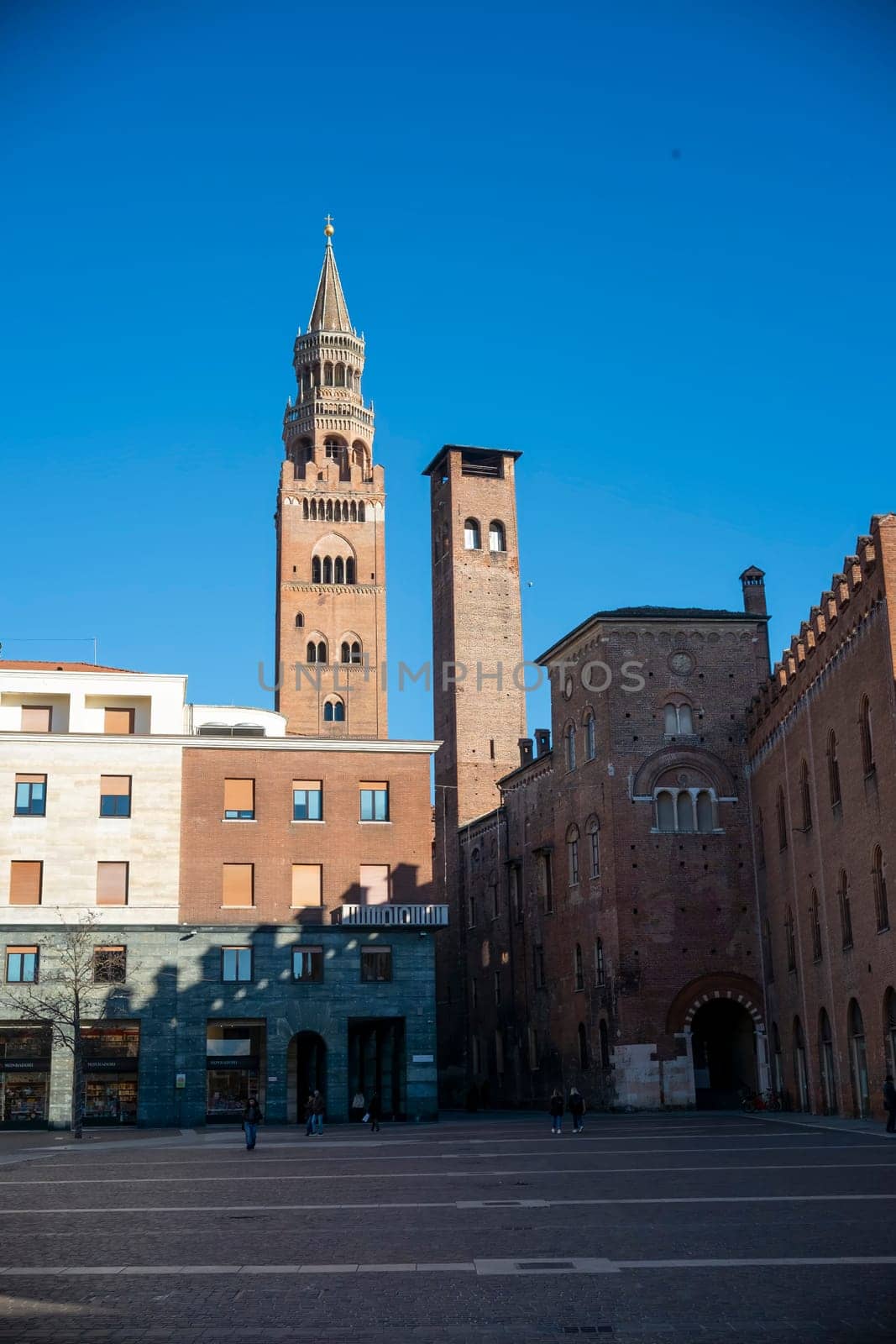 Cremona, Italy - November 27th 2024 The torrazzo bell tower dominates the skyline of cremona, italy, casting a long shadow over piazza del comune on a sunny day
