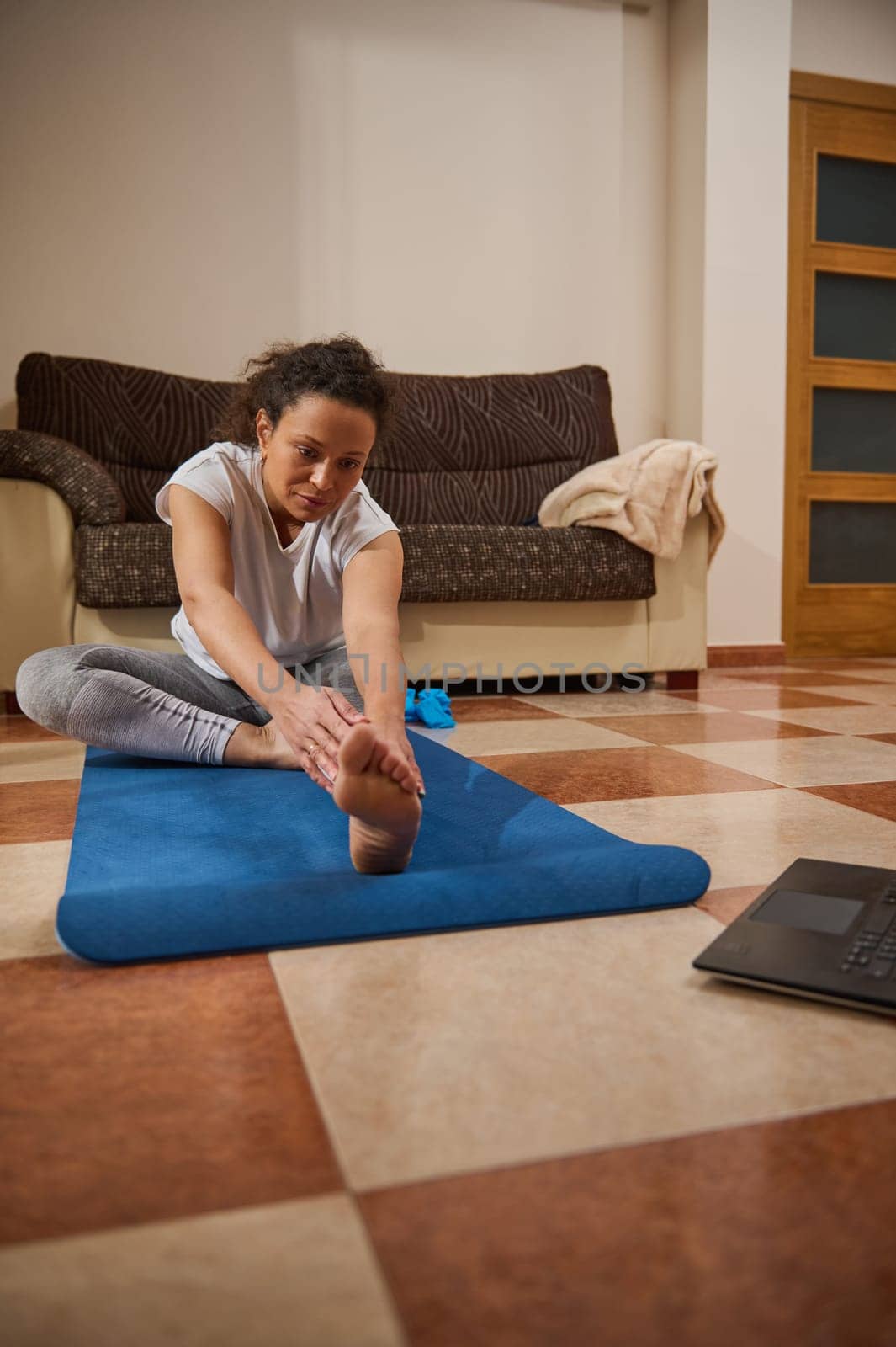 A woman performs yoga on a mat in her living room while following an online session. She is focused and committed to her fitness routine, demonstrating dedication and serenity.