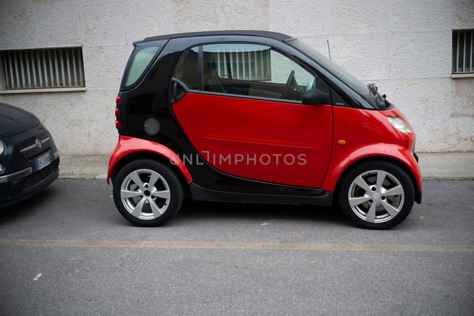 Cremona, Lombardy, Italy - October 27th 2024 A red and black smart fortwo coupe is parked on the side of a street, showcasing its compact size and two-tone design