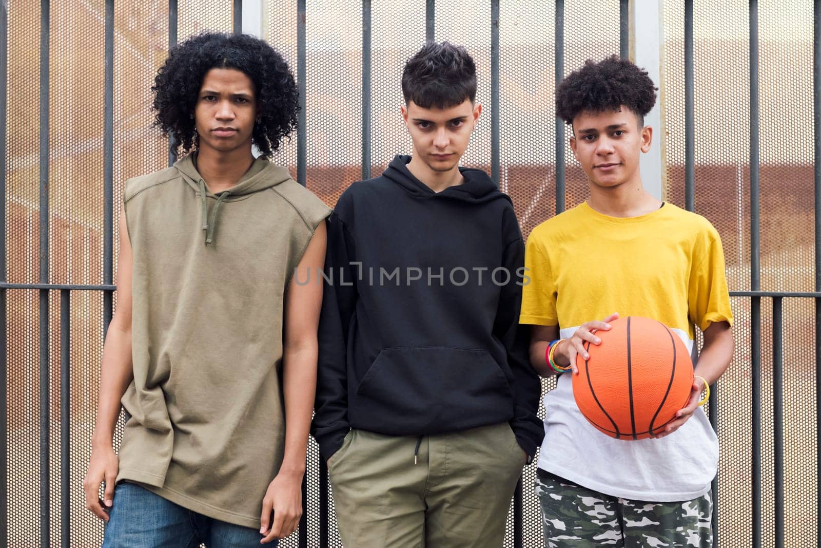 three multiracial male teenagers with basketball standing together on street and looking at camera, concept of friendship and urban lifestyle