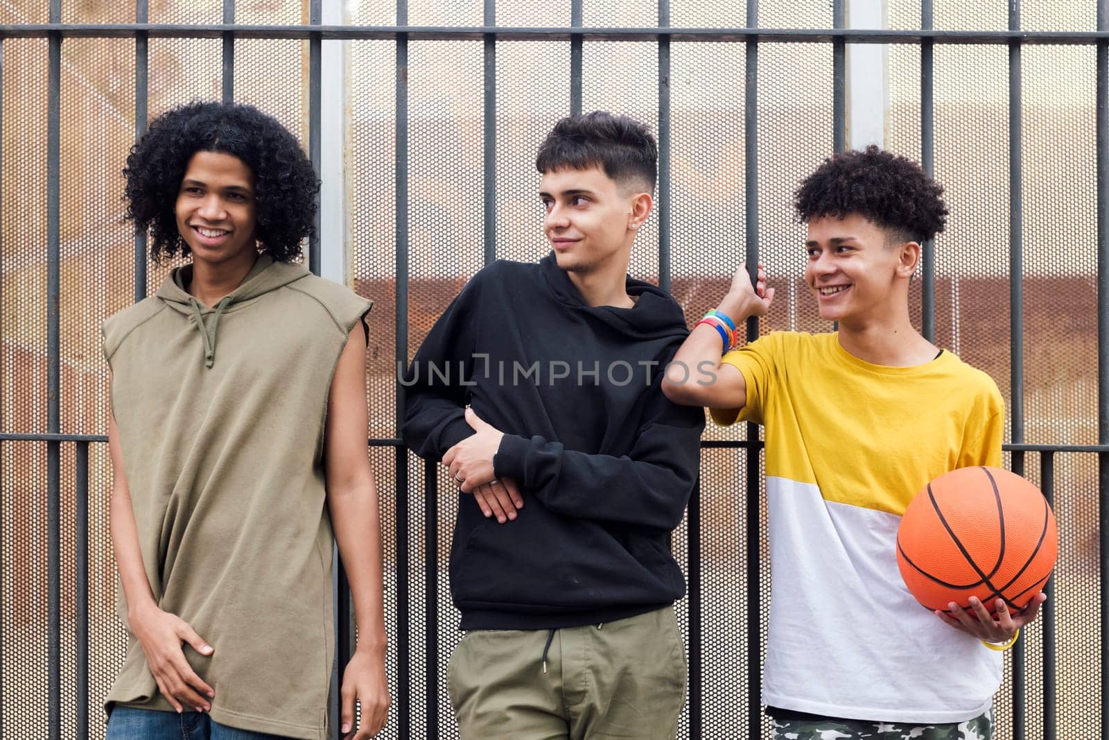 three multiracial male teenagers with basketball smiling happy together on street, concept of friendship and urban lifestyle