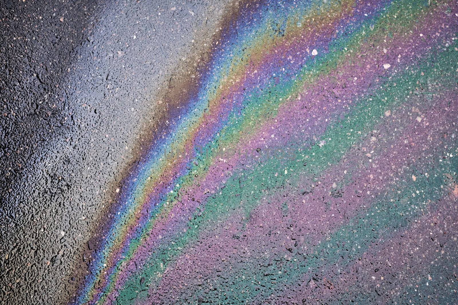 Colorful iridescent trace of oil or gasoline on asphalt surface