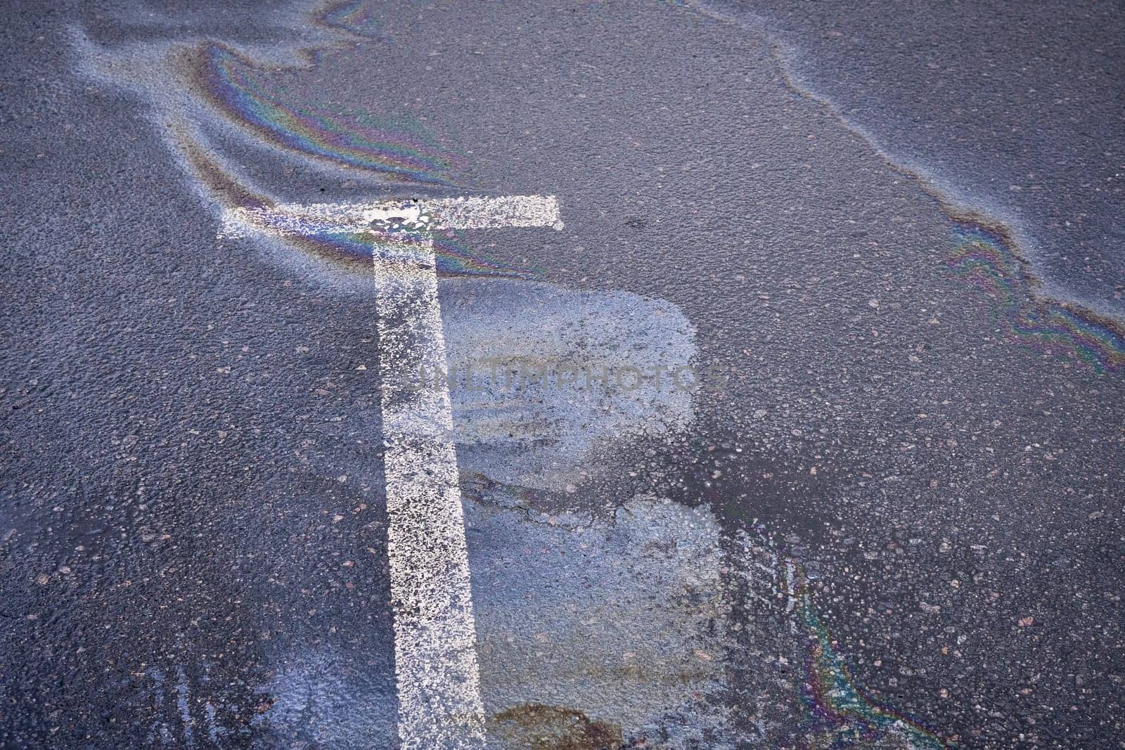 Oil spill on wet asphalt, parking lot with dividing line.