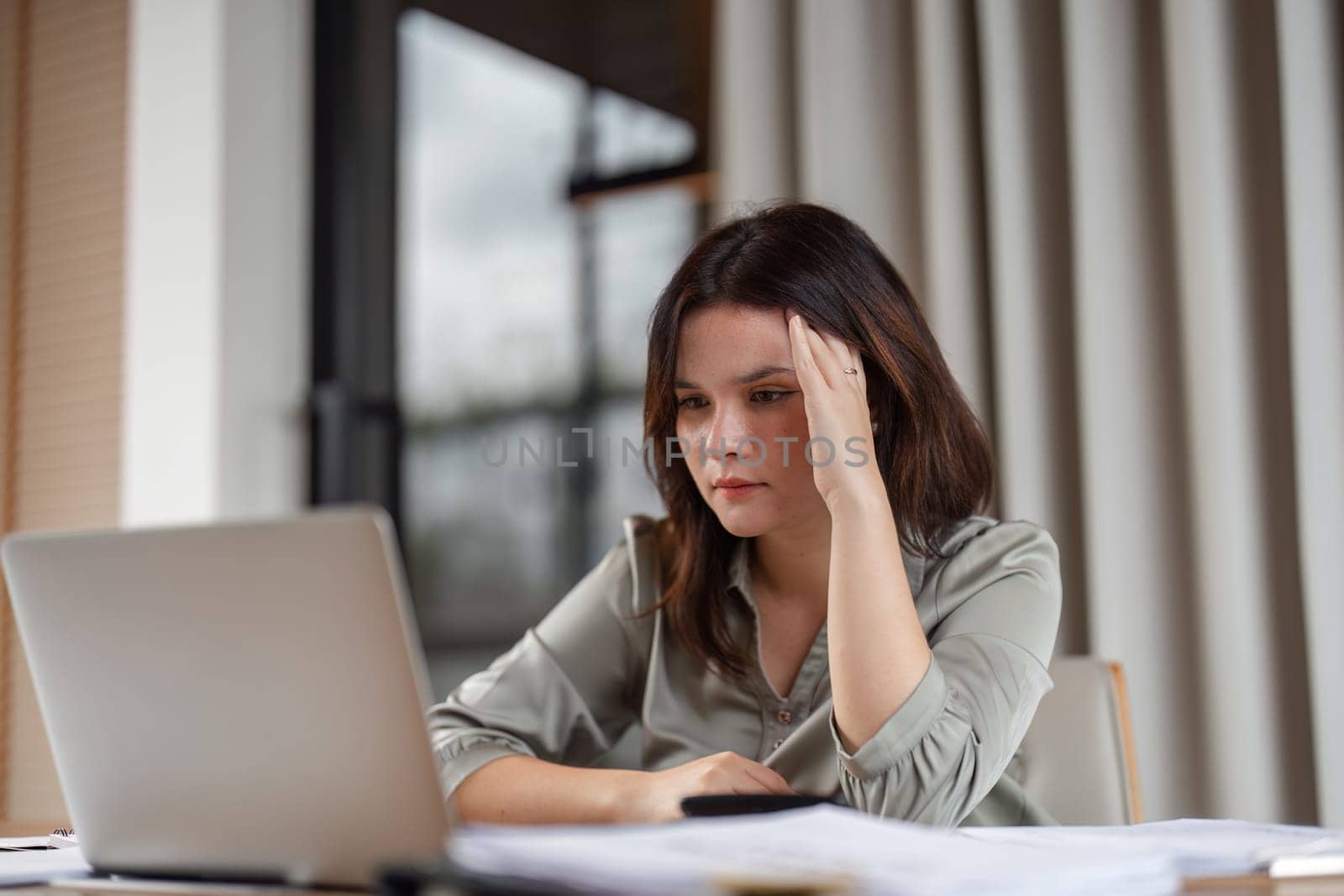A businesswoman experiencing stress at her desk, surrounded by work materials, in a modern office setting.