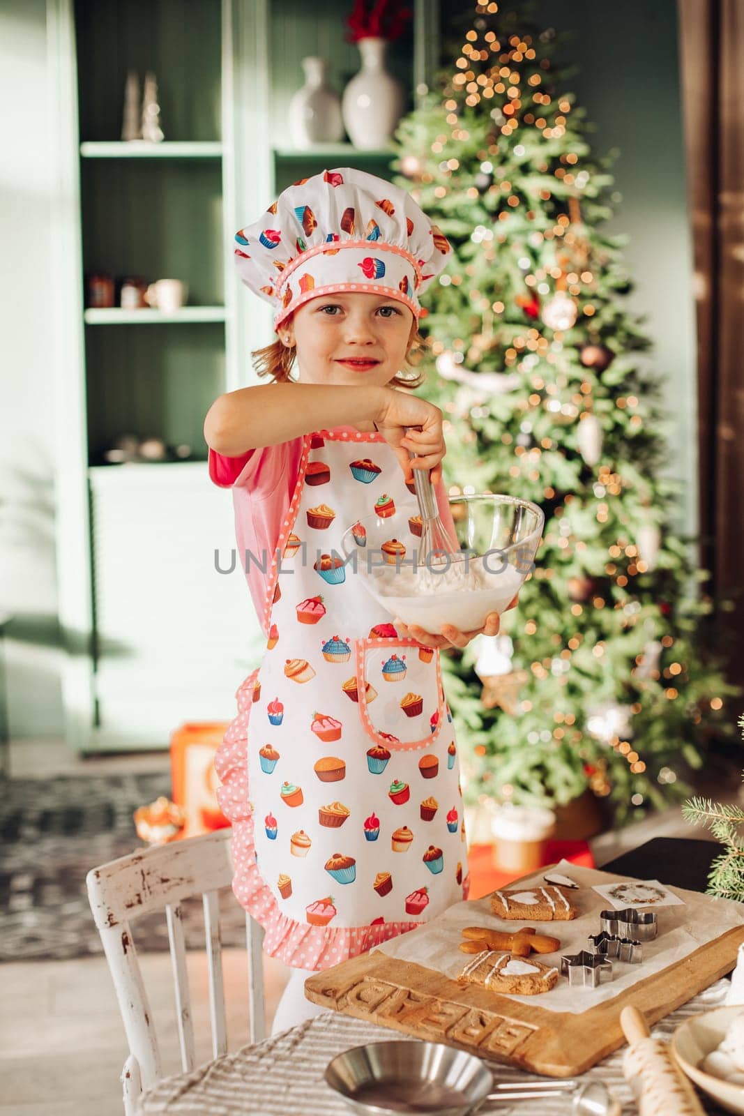 .a girl child in the kitchen with a Christmas tree is preparing or cooking ginger cookies for Christmas or New year