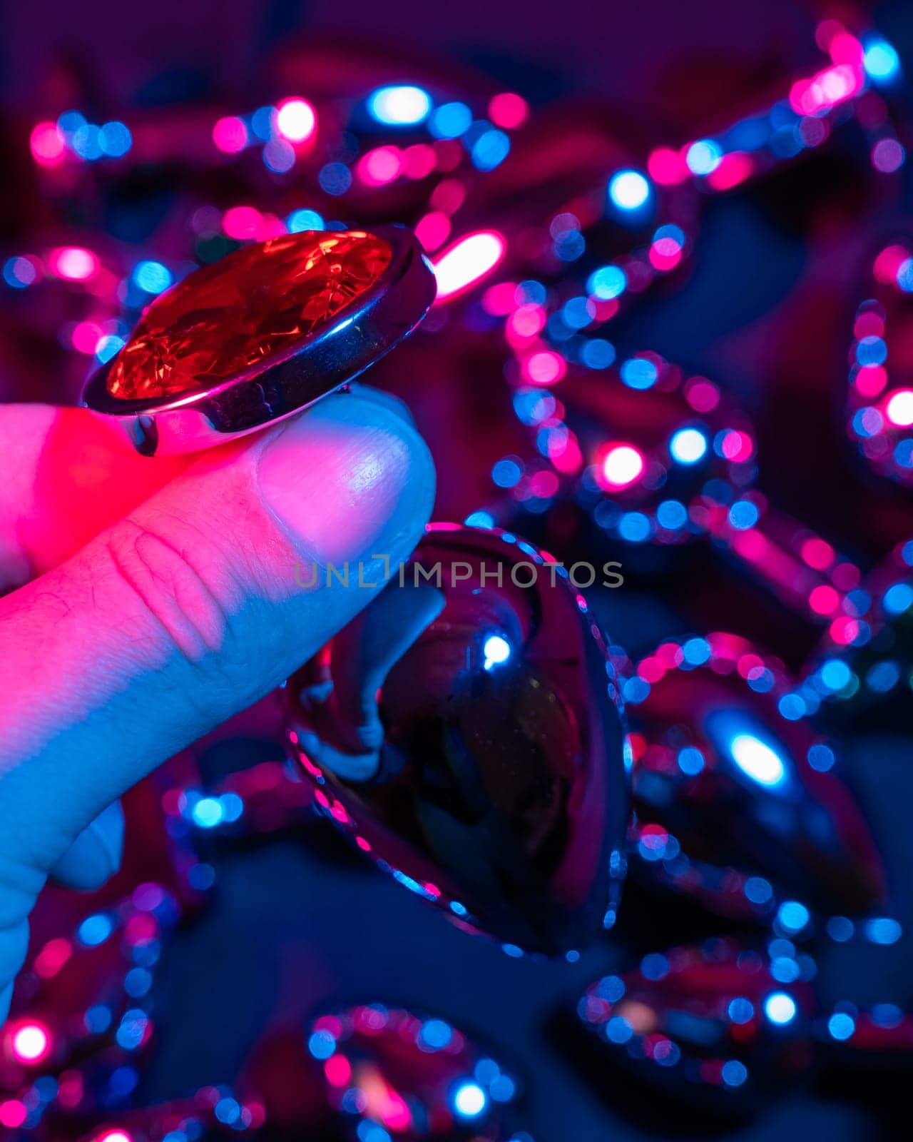 Man holding metal anal plug in neon pink purple light. by mrwed54